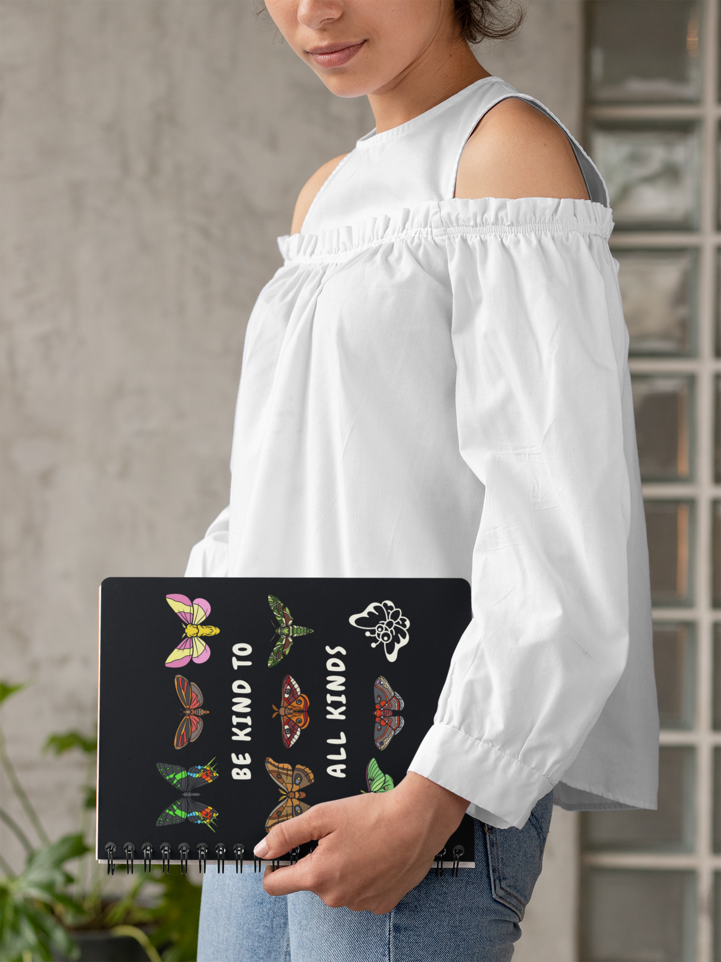 Person holding a 'be kind to all kinds' spiral notebook featuring moths and butterflies