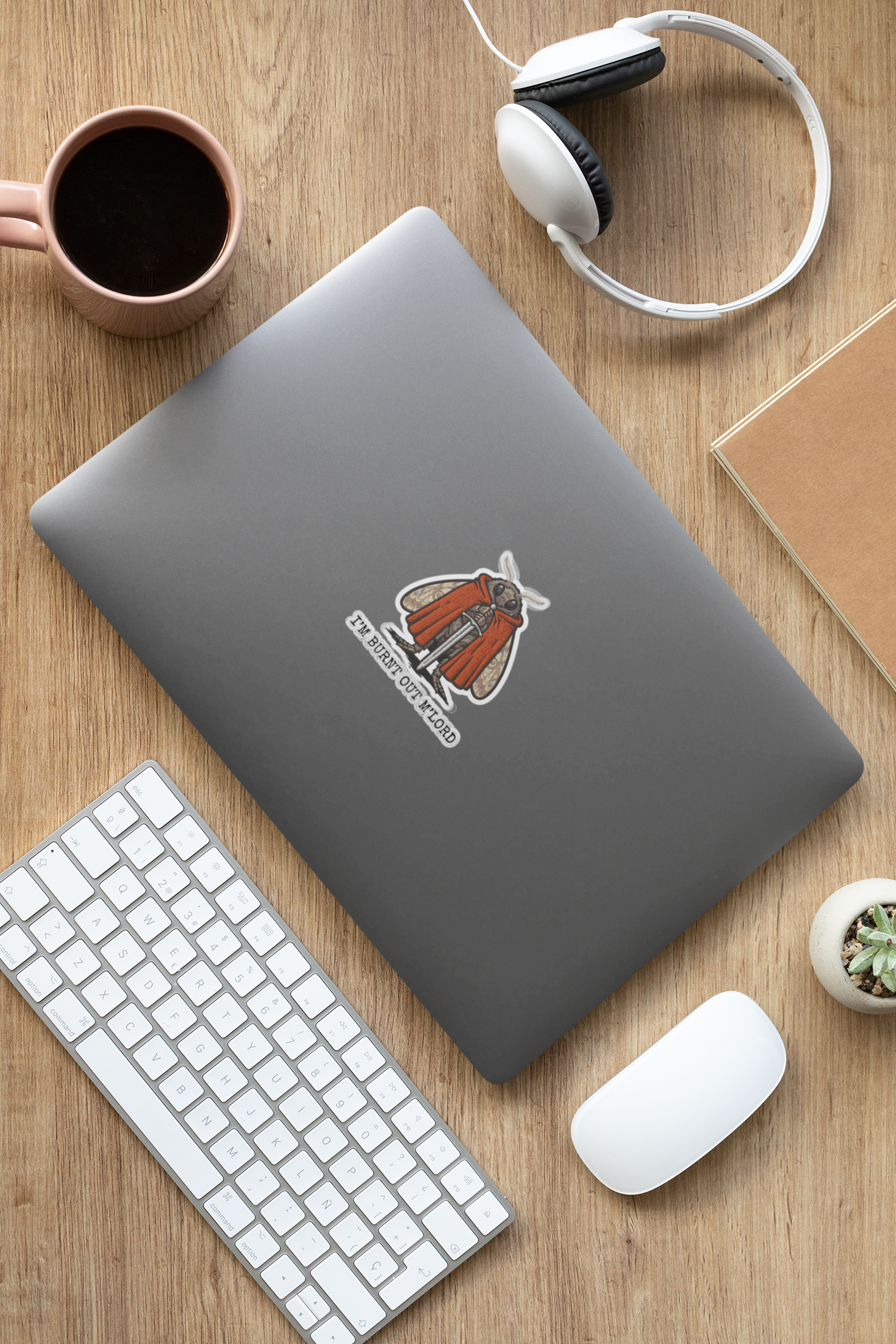 Gray laptop with a moth meme burnout sticker on a wooden desk with keyboard, mouse, and coffee cup.