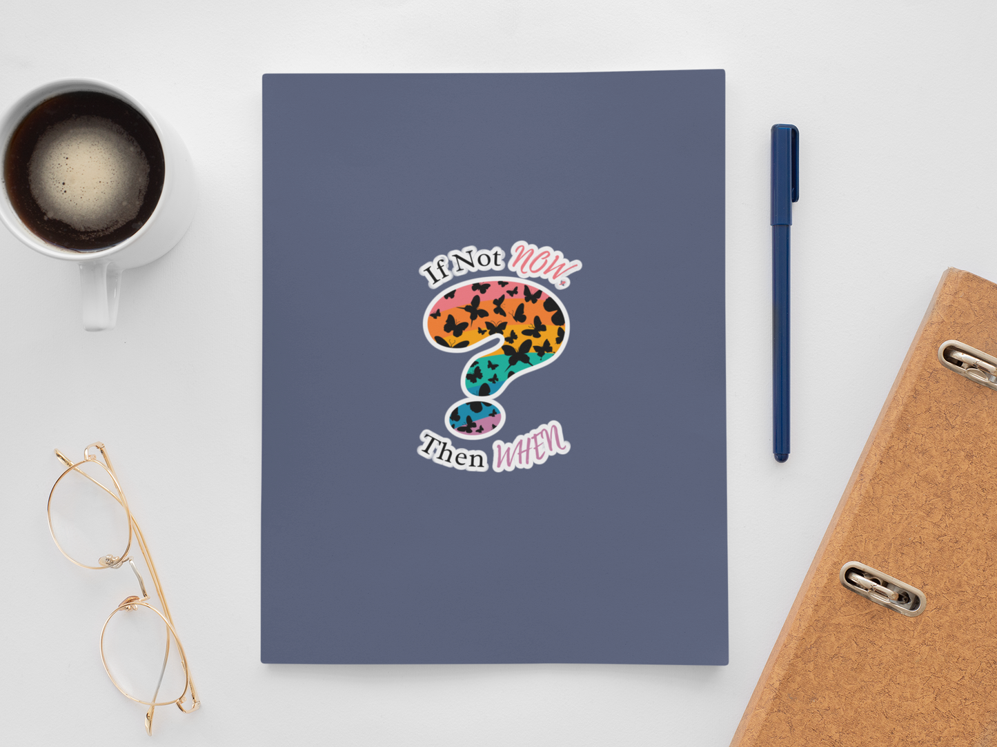 notebook with a rainbow question mark sticker on a desk with glasses, pen, and coffee cup.