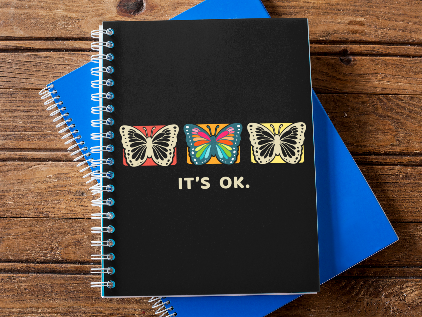 it's ok butterfly notebook on a wooden desk next to blue pads, flat-lay