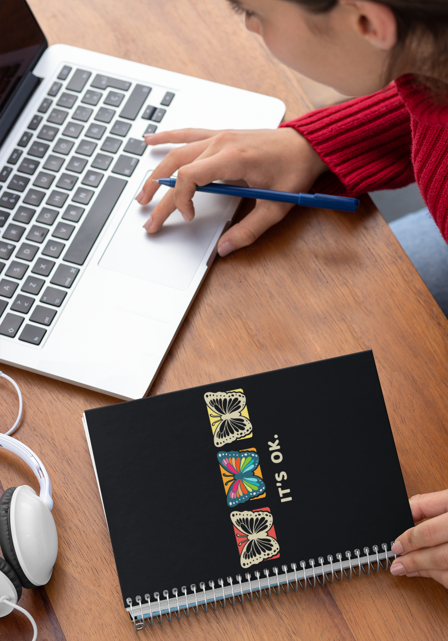 person writing in the it's ok butterfly affirmation notebook beside a laptops