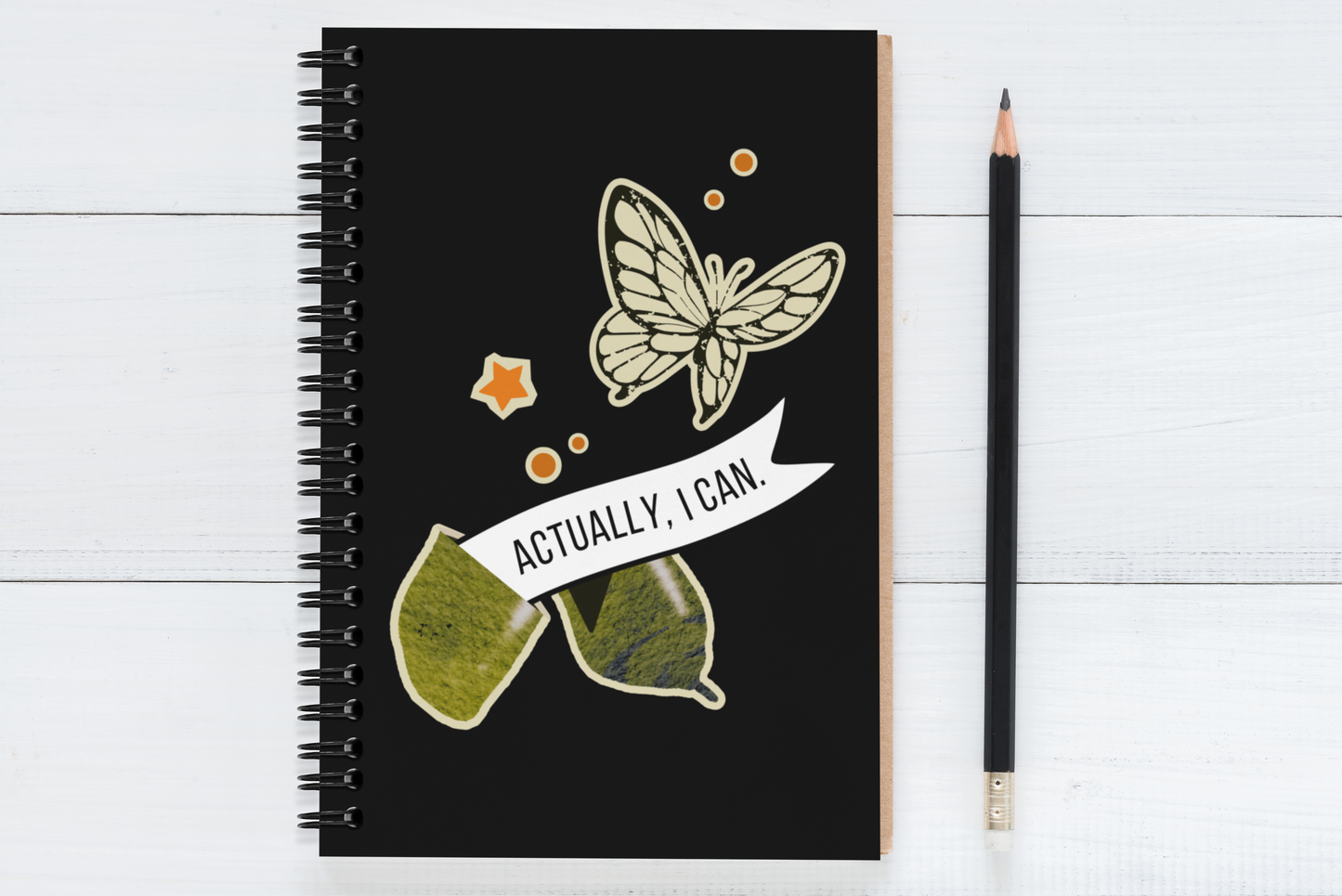 notebook with butterfly design and 'actually, i can' text on a white wooden surface