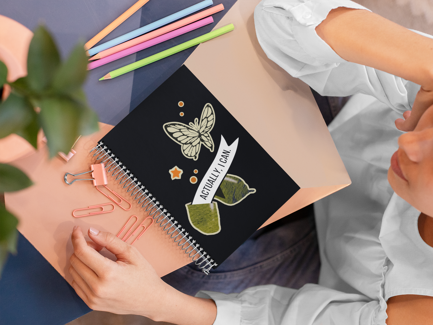 person holding a notebook with butterfly design and stationery items on a desk