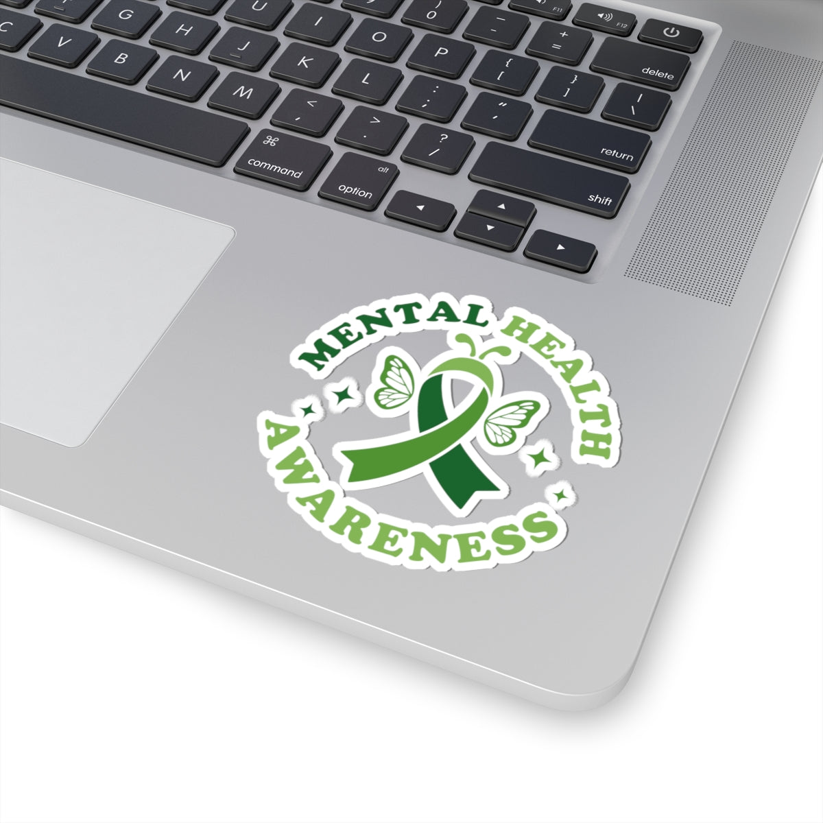 Glossy mental health awareness butterfly sticker with green ribbon design placed on a silver laptop near the keyboard.