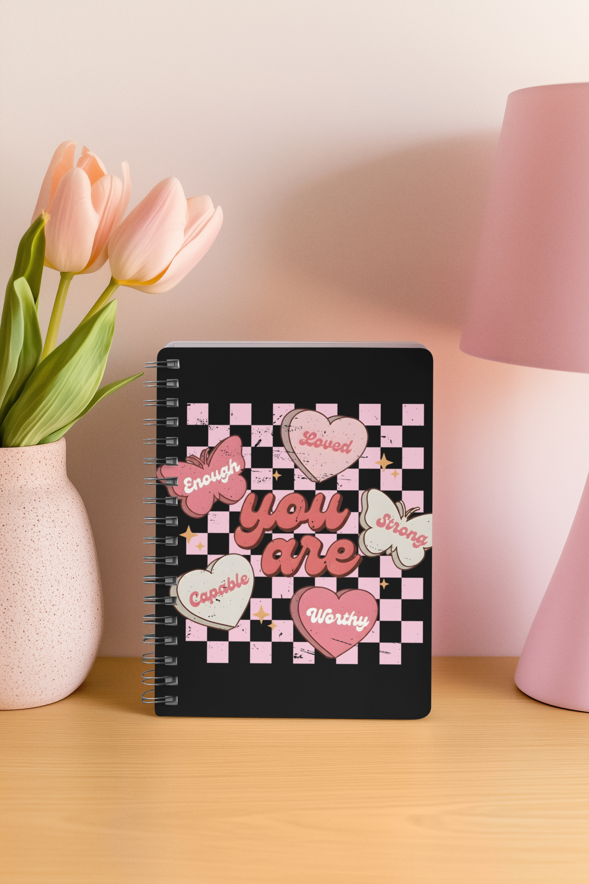 Butterfly affirmation spiral notebook with motivational quote on a table with a vase of tulips and a lamp in the background