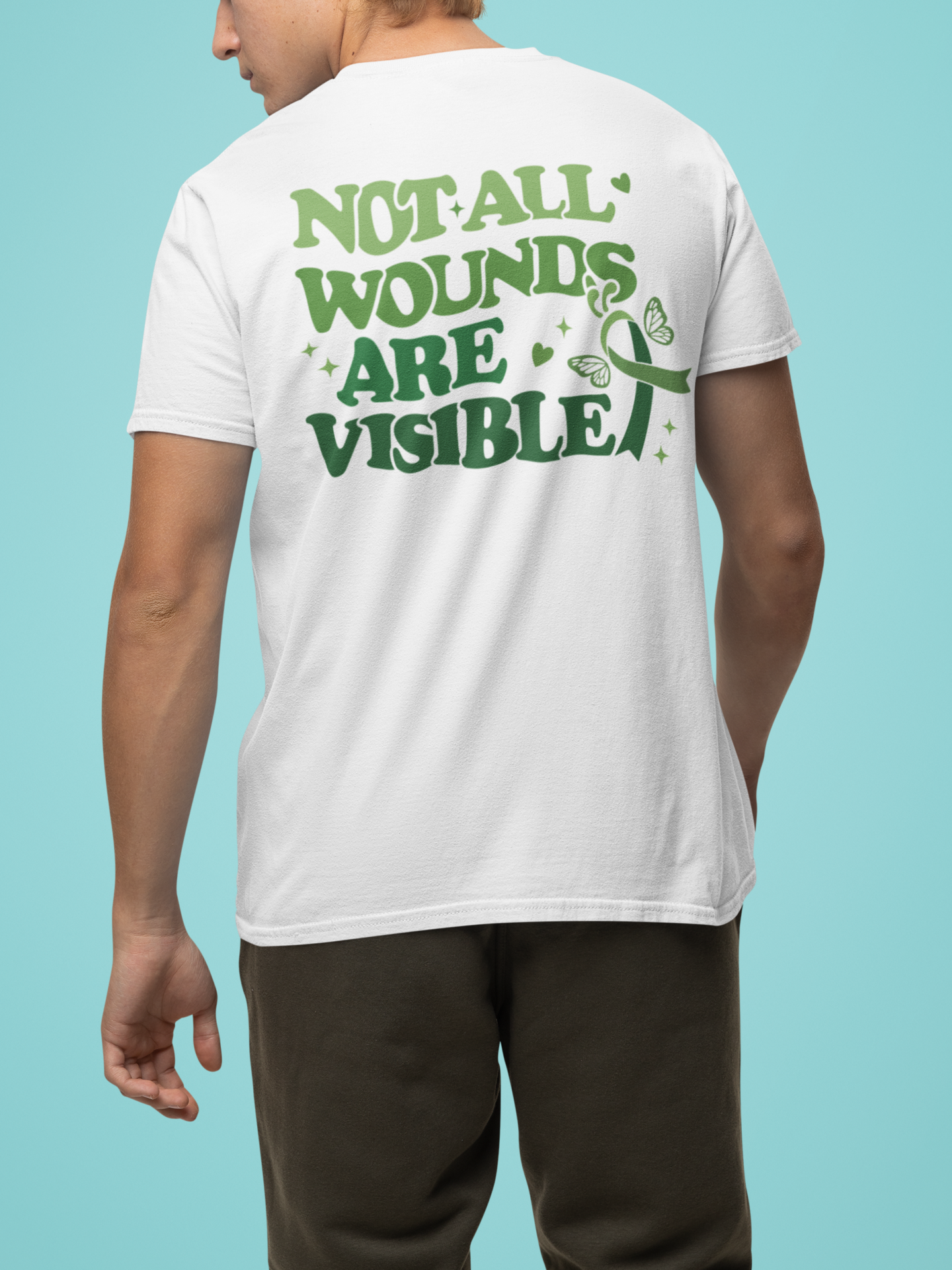 Man wearing a white mental health awareness t-shirt with a large green “Not All Wounds Are Visible” butterfly and green ribbon design on the back.