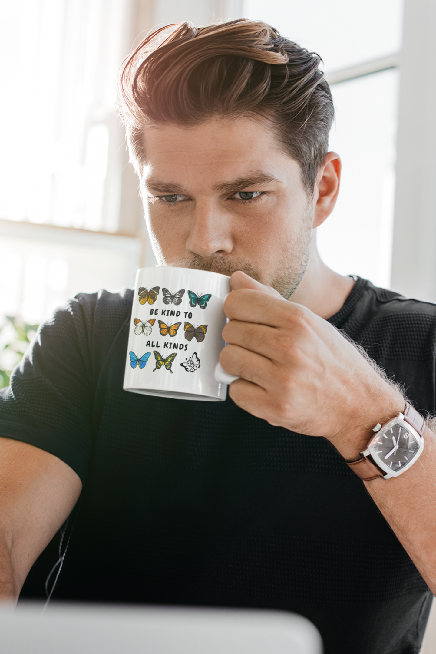 man holding and sipping rom "be kind to all kinds" kindness mug at desk, sitting indoors