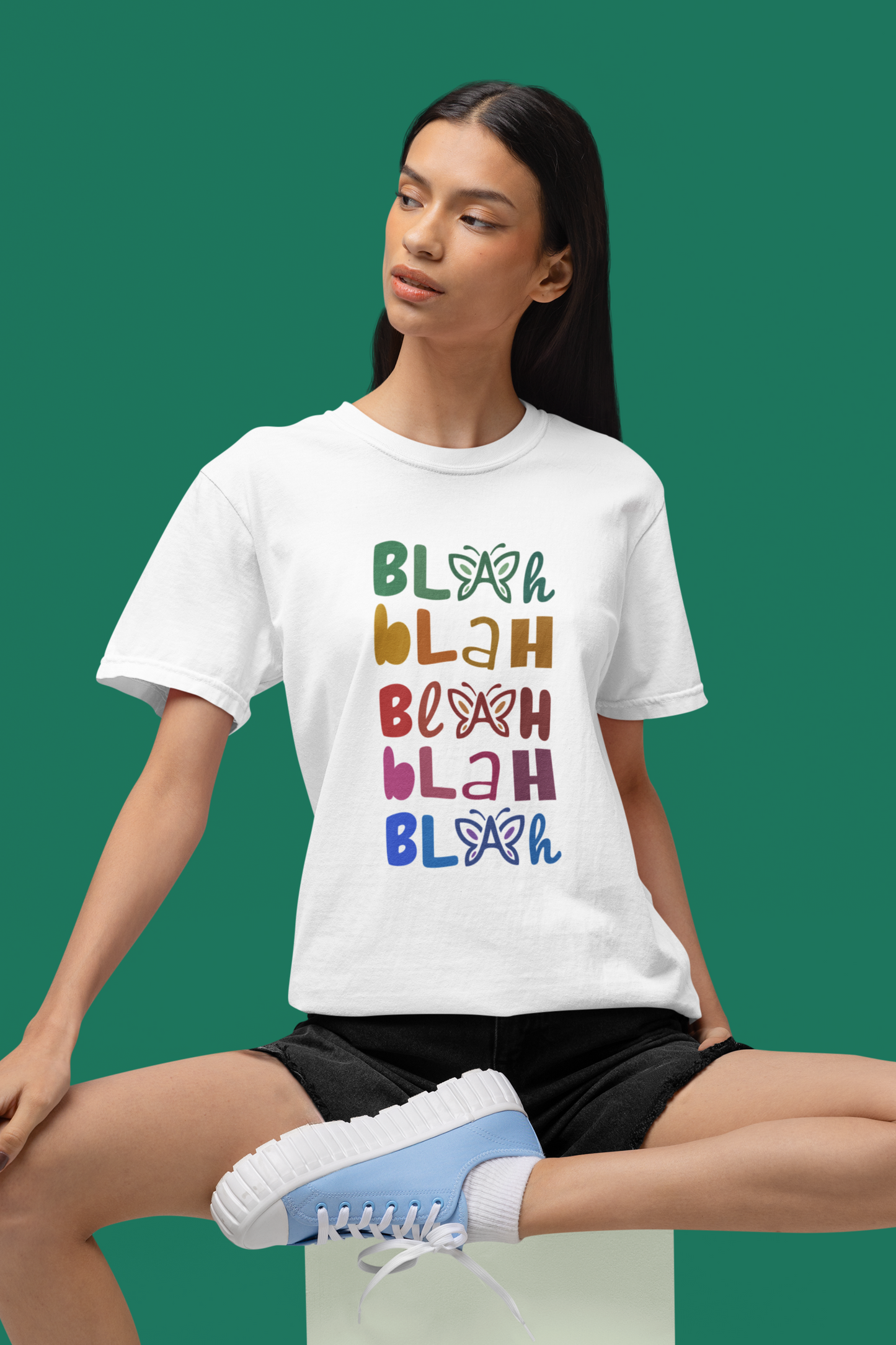 Female model wearing a white t-shirt with butterflies and colorful “Blah Blah Blah” text design on a green background