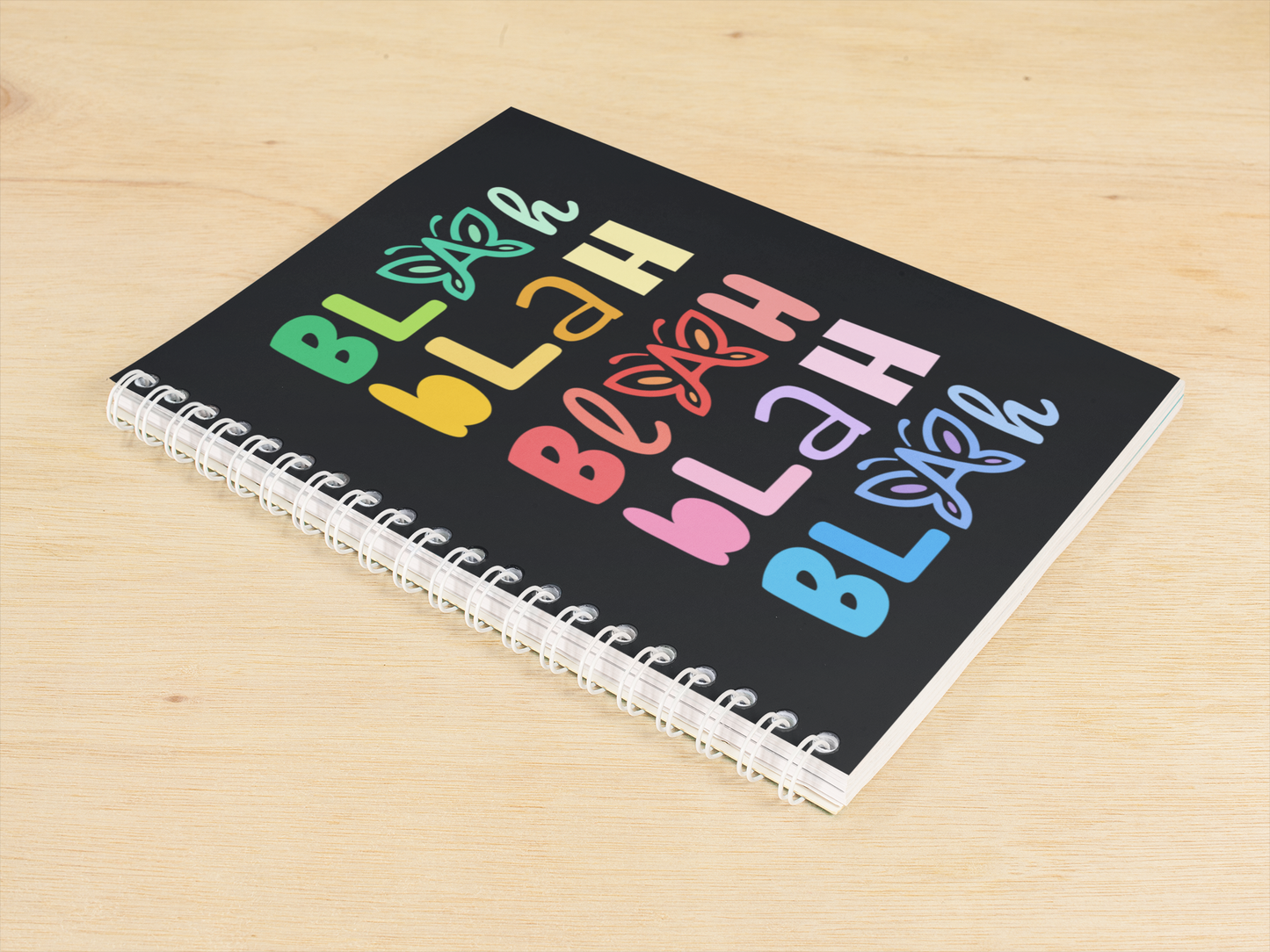 Notebook with colorful “Blah Blah Blah” text and butterfly graphics on a wooden surface