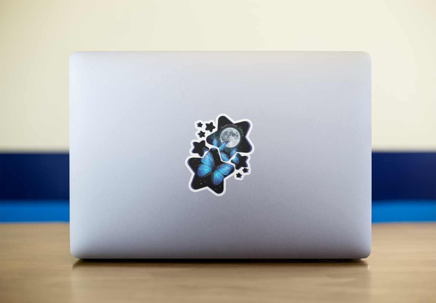 Laptop with a blue morpho butterfly celestial moon and stars vinyl sticker on a wooden surface with a blue and beige background