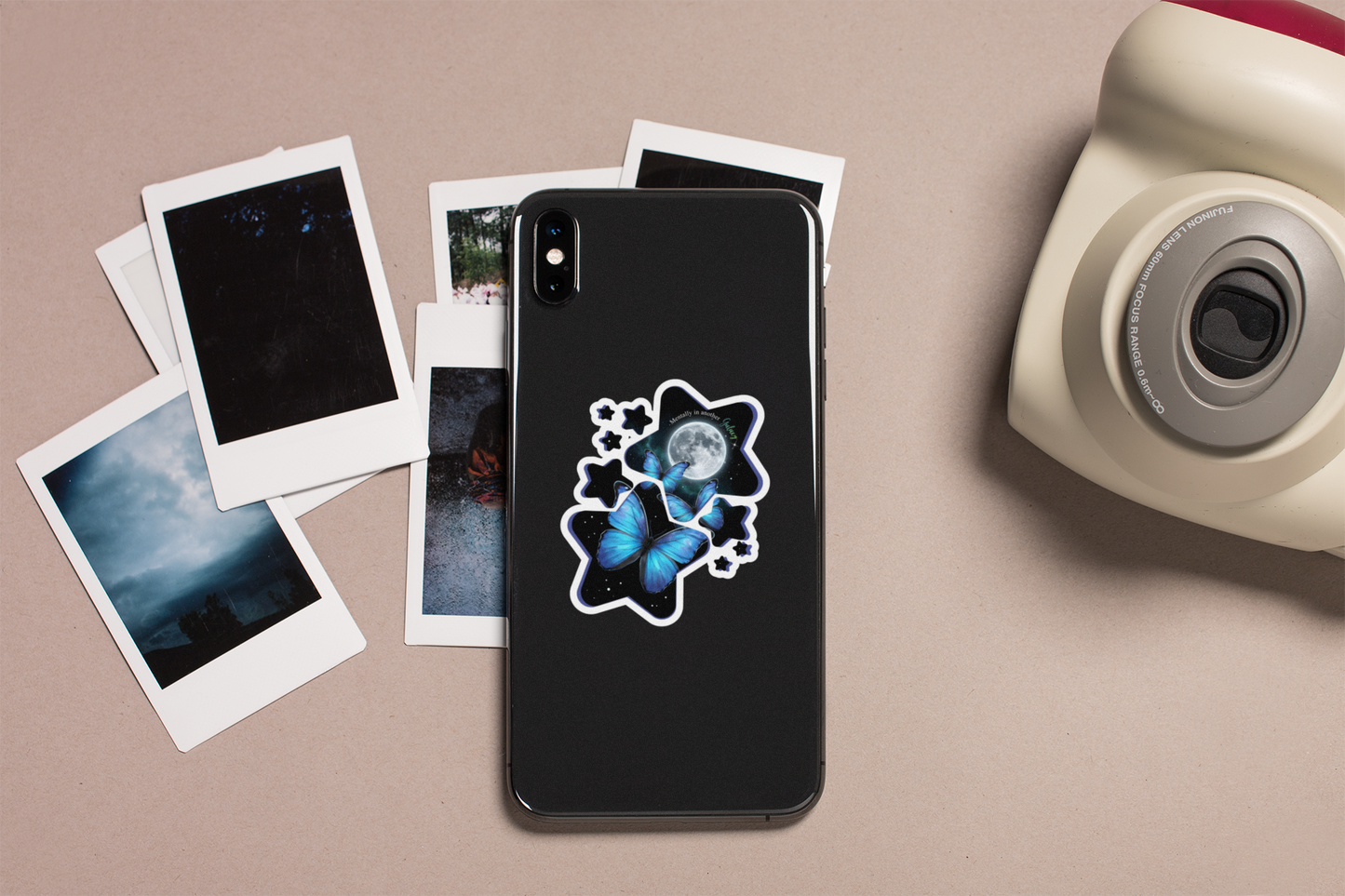 Phone case with a blue morpho butterfly celestial moon and stars sticker on a beige surface with photos and a camera.