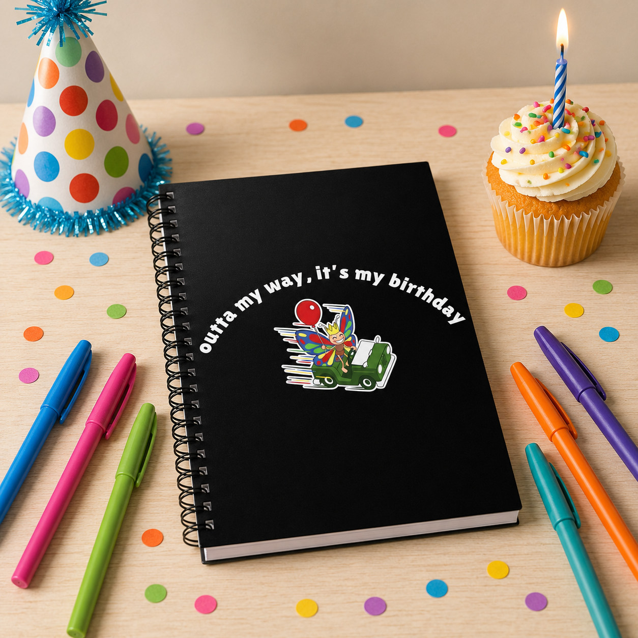 Butterfly birthday spiral notebook on a party table with colorful pens, birthday hat, cupcake, candle, and confetti.