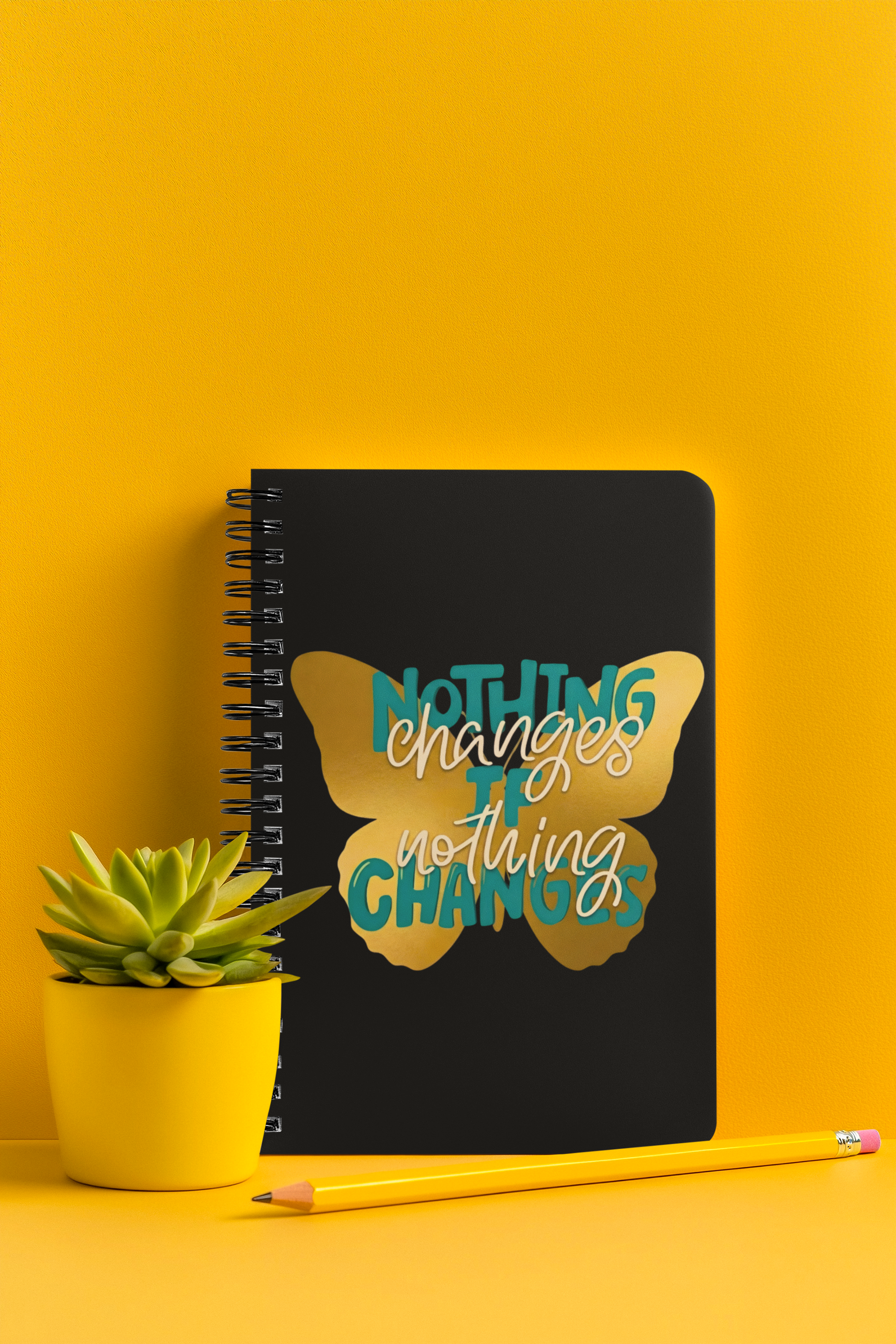 Inspirational butterfly motivational notebook displayed on a yellow desk with plant and pencil.