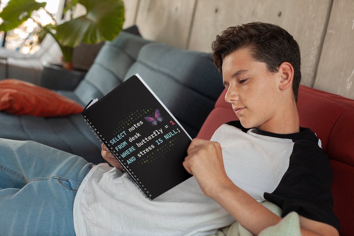 young boy sitting on a couch reading a 6x8 notebook with sql programming text and butterfly pixel art graphic