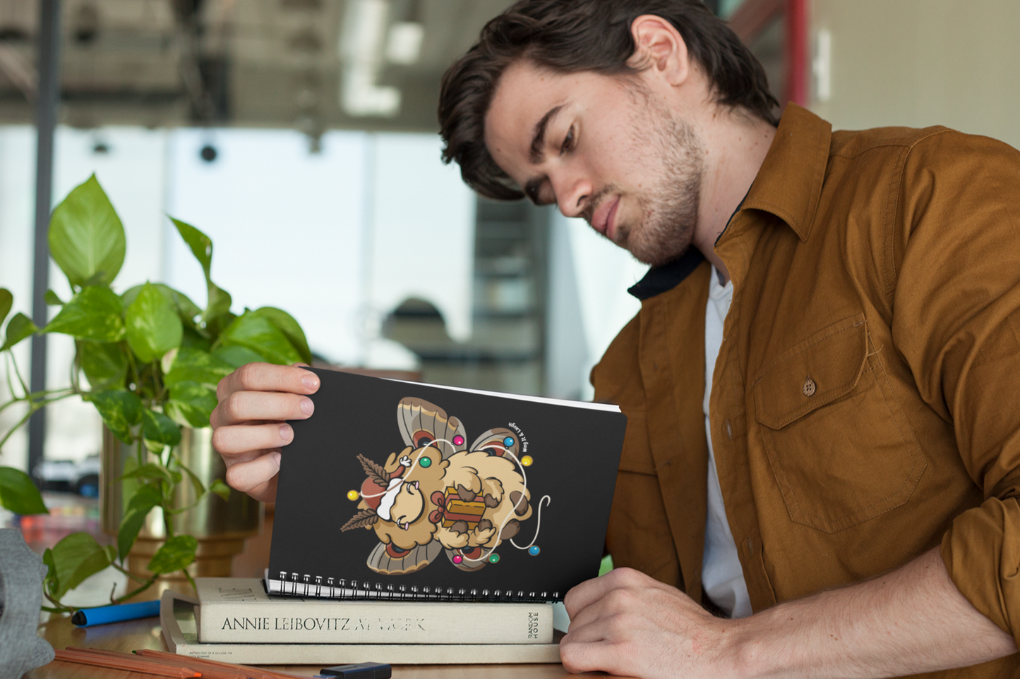 Person holding a cozy holiday moth spiral notebook on a desk.