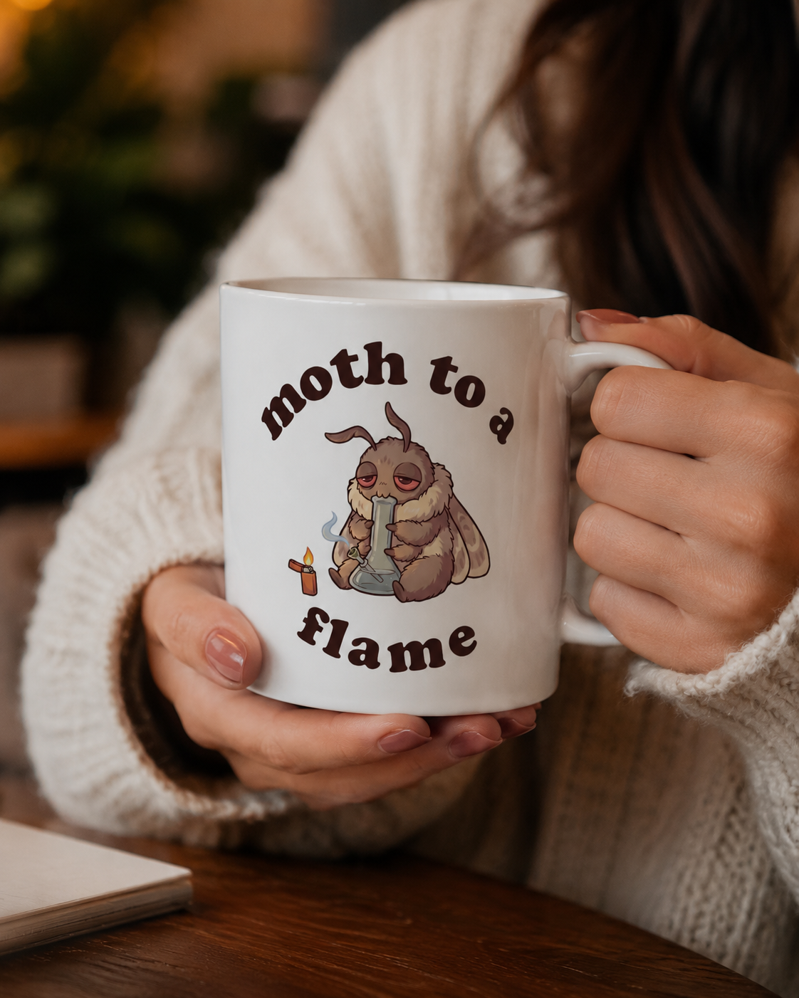 Cozy white Moth To a Flame weed coffee mug held indoors, featuring a sleepy moth with bong and lighter for cannabis lovers and stoner animal fans.
