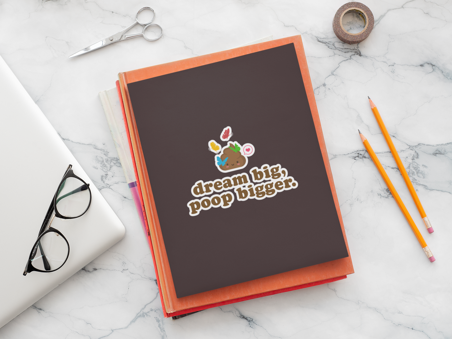 notebook with 'dream big, poop bigger' poop sticker on a marble surface with writing tools