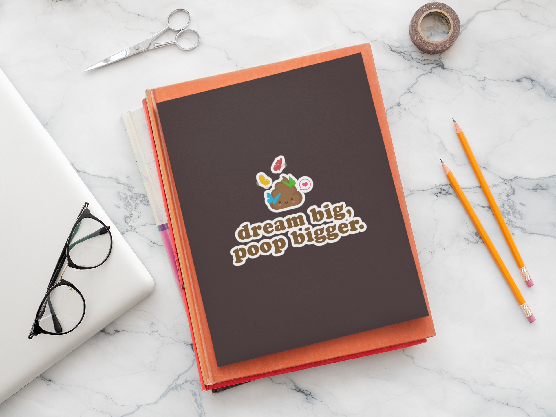 notebook with 'dream big, poop bigger' poop sticker on a marble surface with writing tools