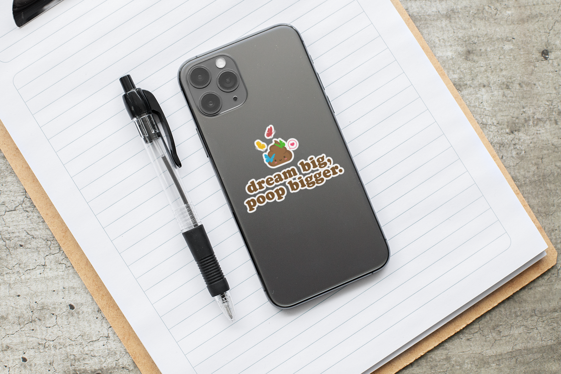 "dream big, poop bigger" sticker on phone over a notebook with a pen