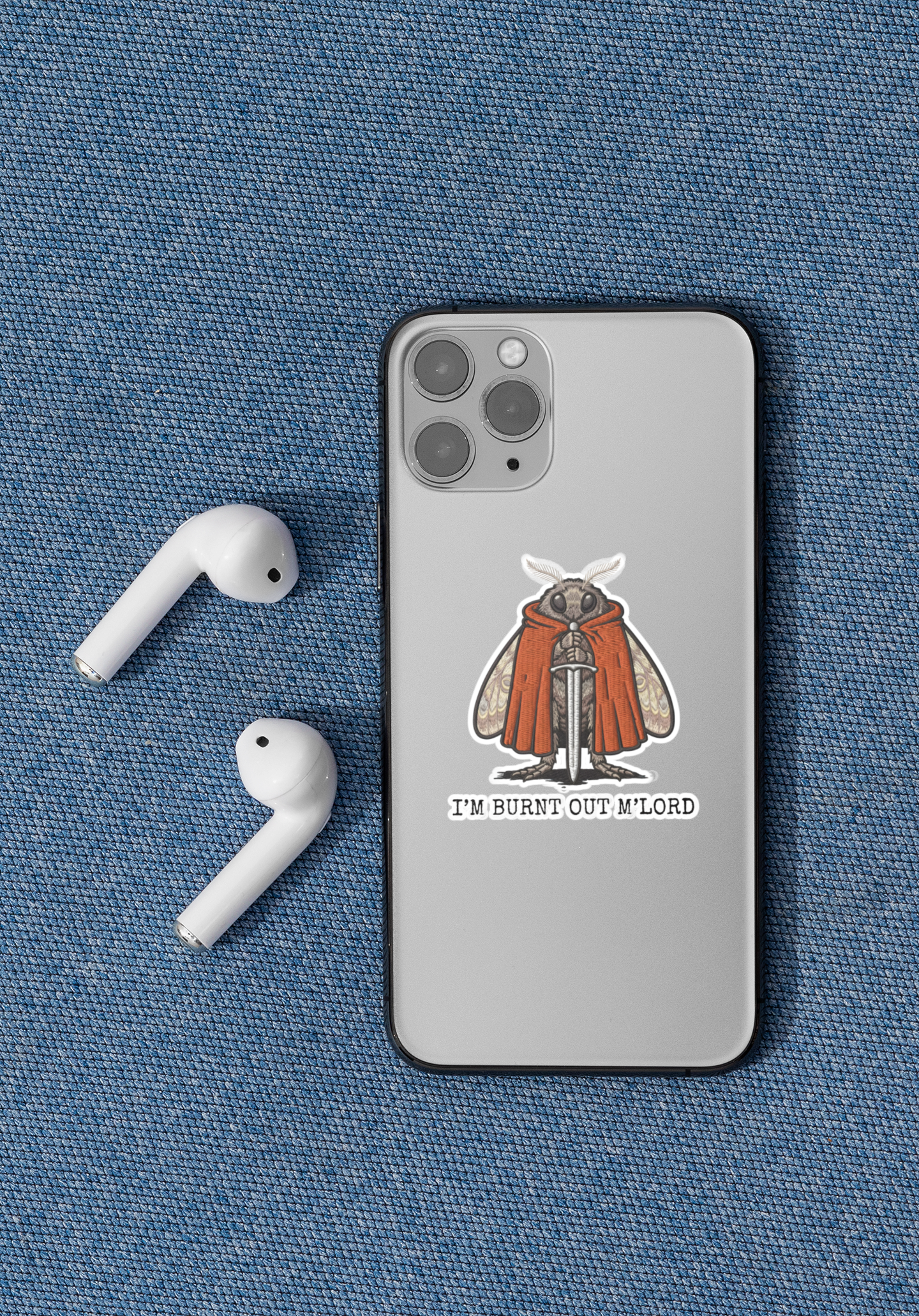 Phone case with a im burnt out mlord moth sticker, accompanied by airpods on a blue fabric background.