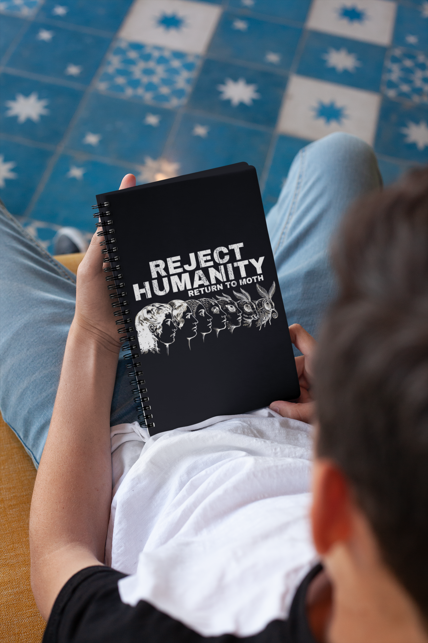 Person holding a funny moth meme notebook on a patterned floor.