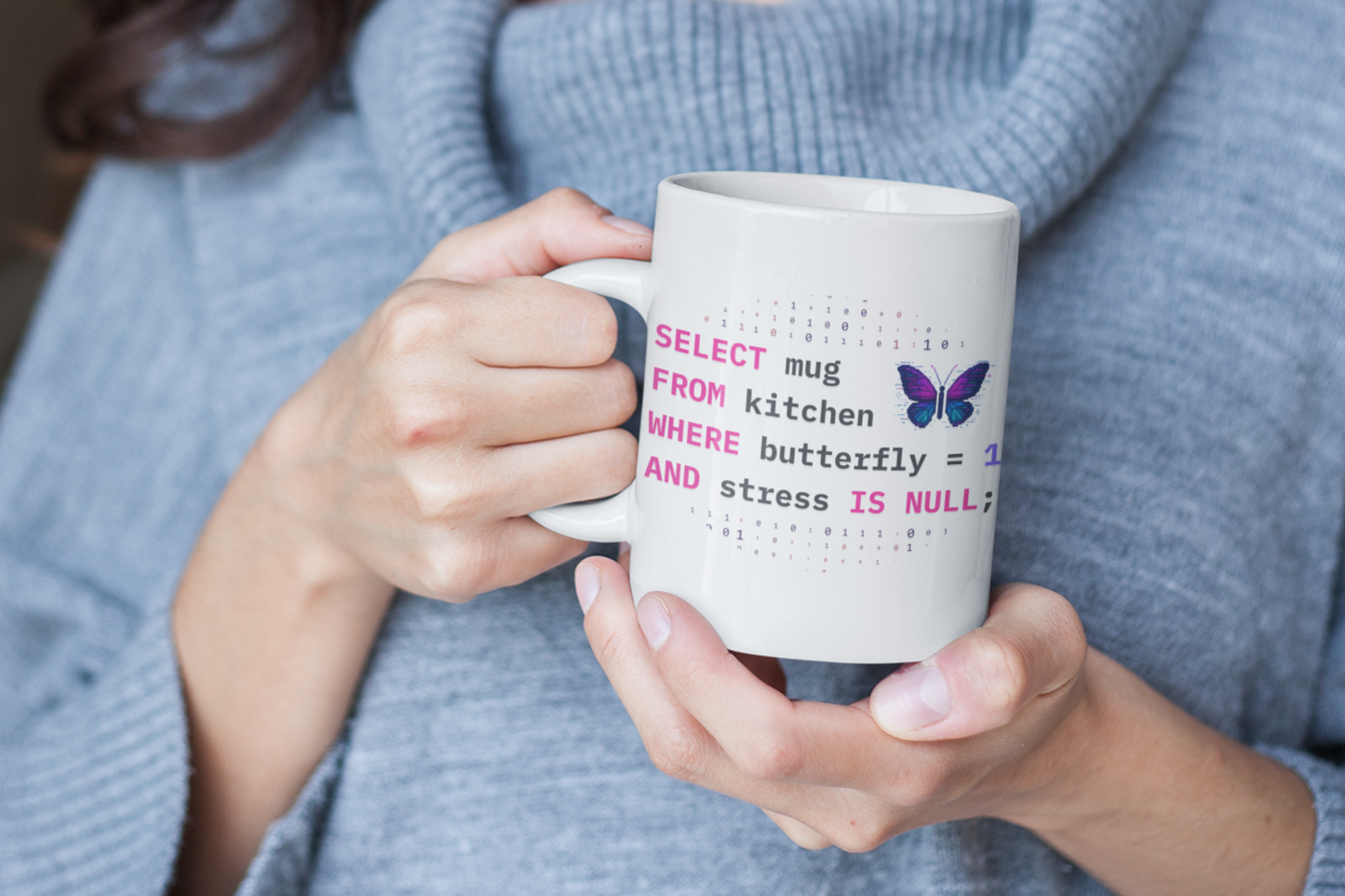 person holding a pixel art butterfly ceramic mug, featuring SQL coding language and a butterfly graphic, wearing a gray sweater