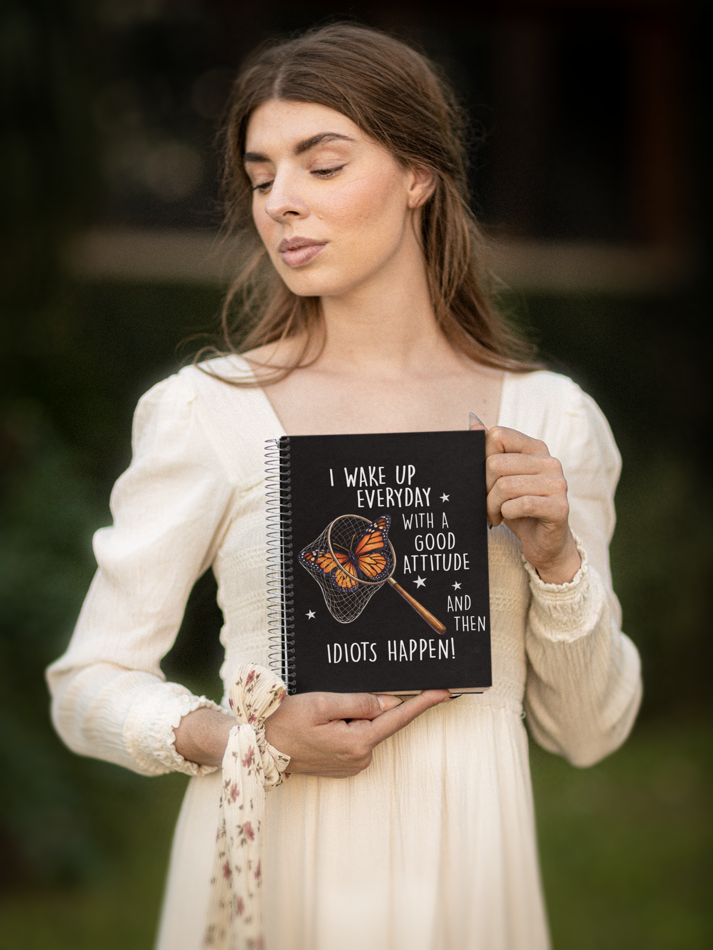Woman holding black butterfly humor notebook with sarcastic quote design outdoors