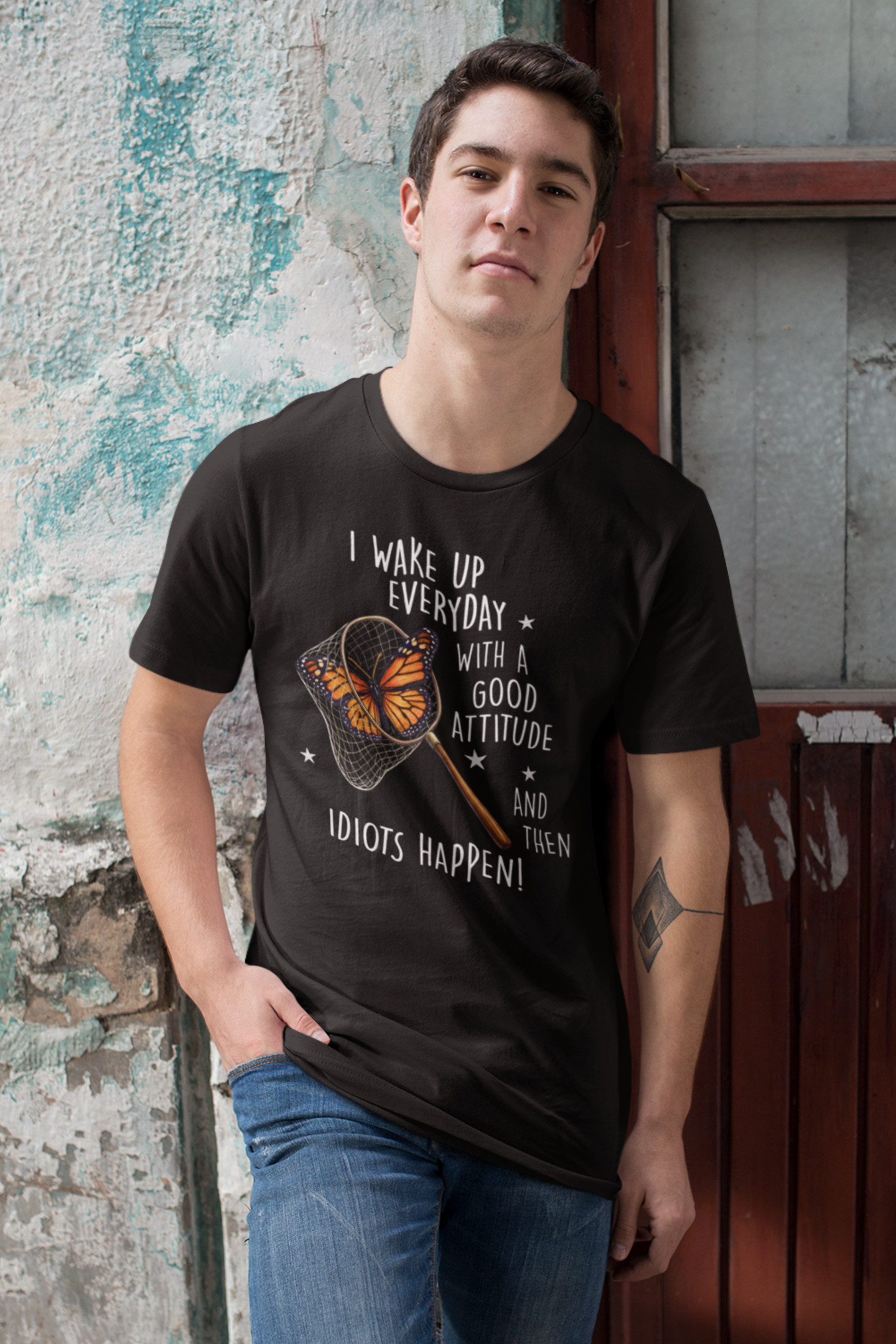 Male model wearing black funny butterfly t-shirt with sarcastic quote and butterfly net graphic, standing against a textured wall.