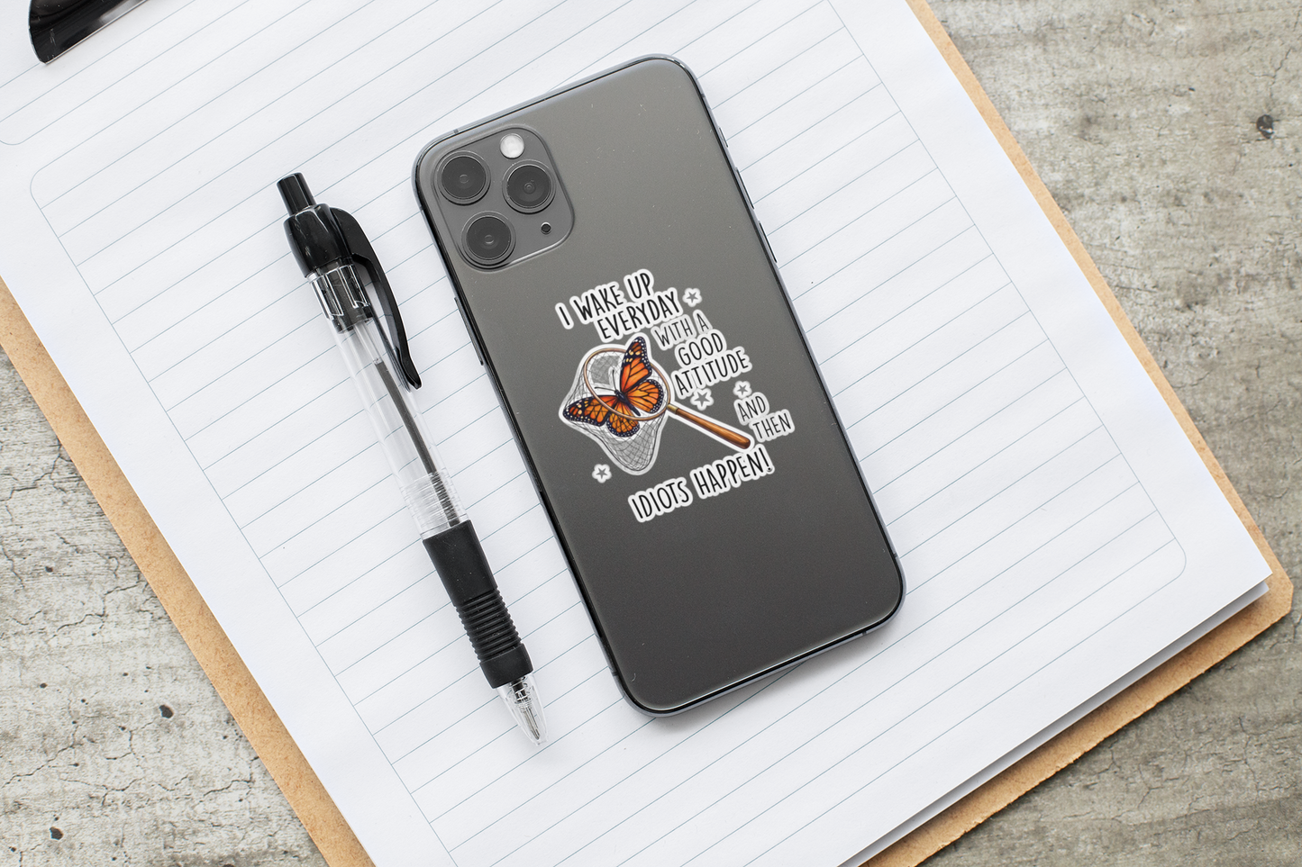 Funny butterfly sticker applied to a phone case on top of a notebook with a pen