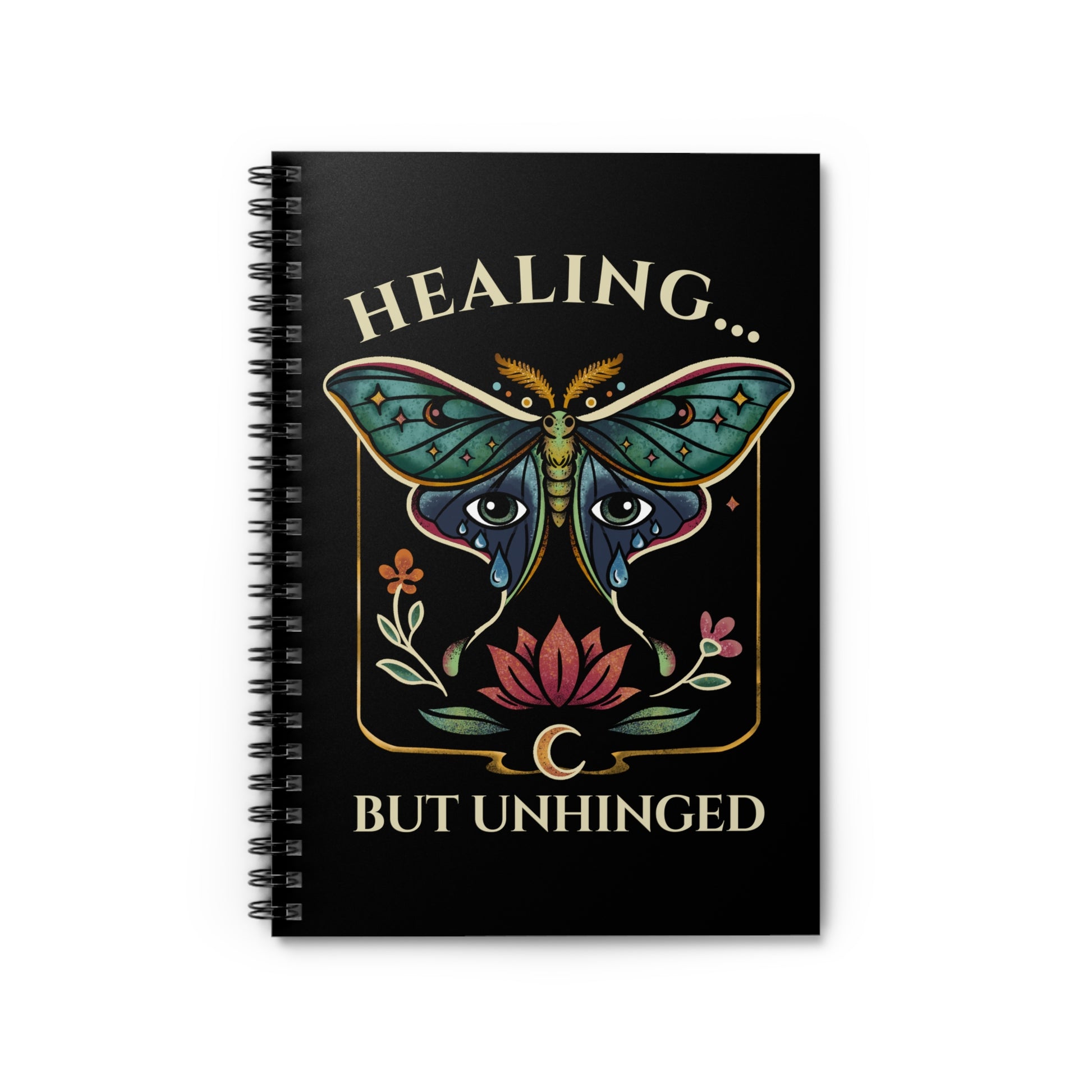 a spiral notebook with a black cover featuring a bold illustration of a luna moth with teary eyes and a blossoming lotus