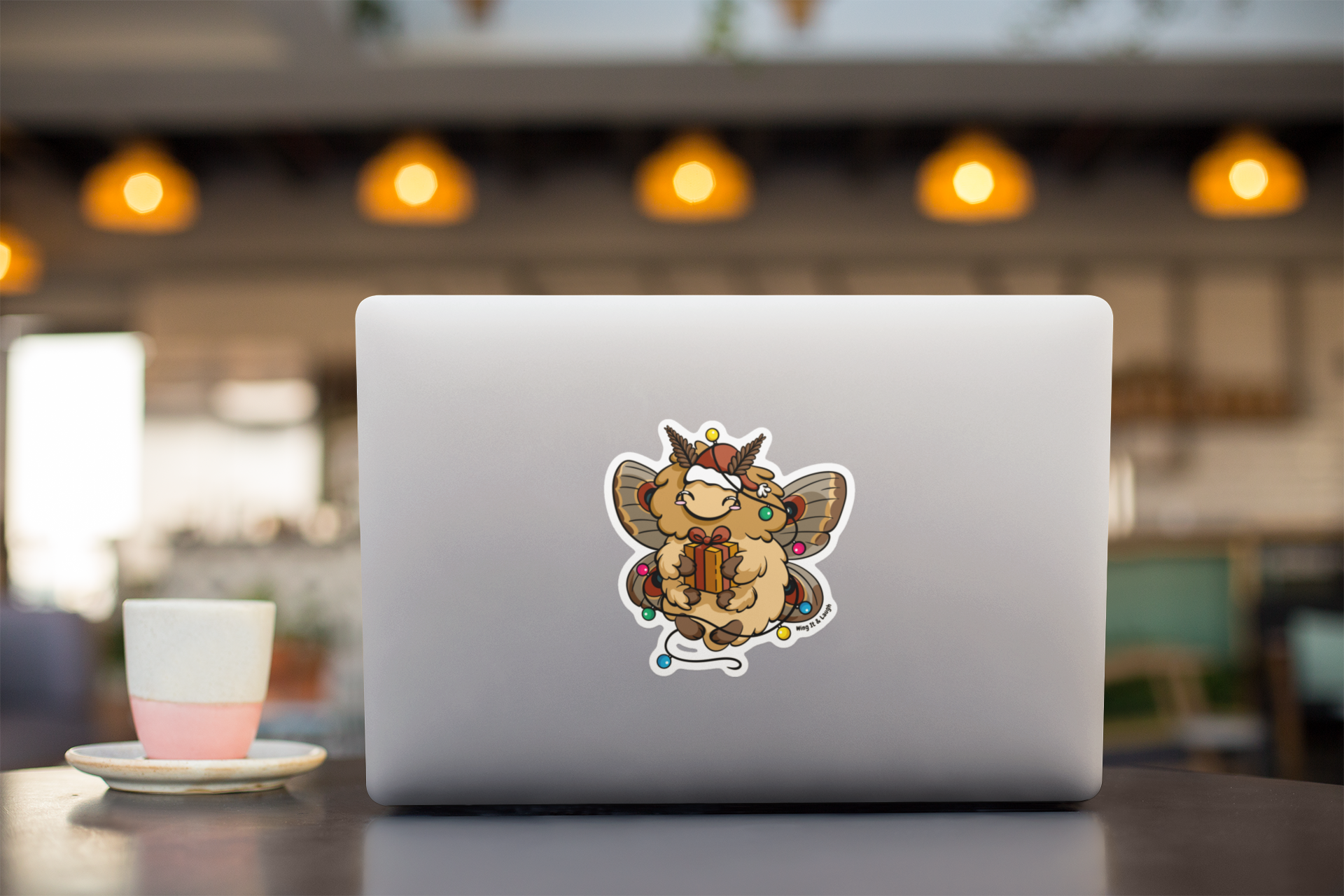 Laptop with a cute Christmas holiday moth vinyl sticker on a blurred cafe background