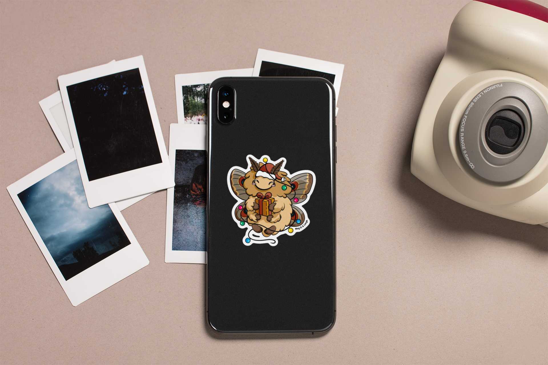 Phone case with cute Christmas holiday moth sticker on a table with photos and a camera.