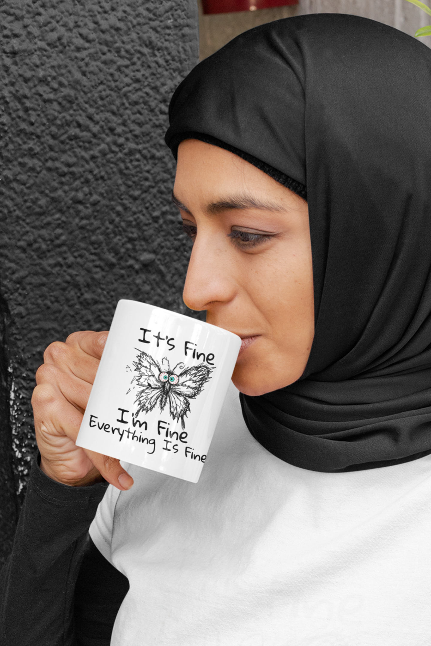 Woman drinking from It's Fine I'm Fine Everything Is Fine butterfly anxiety humor mug, standing outdoors.