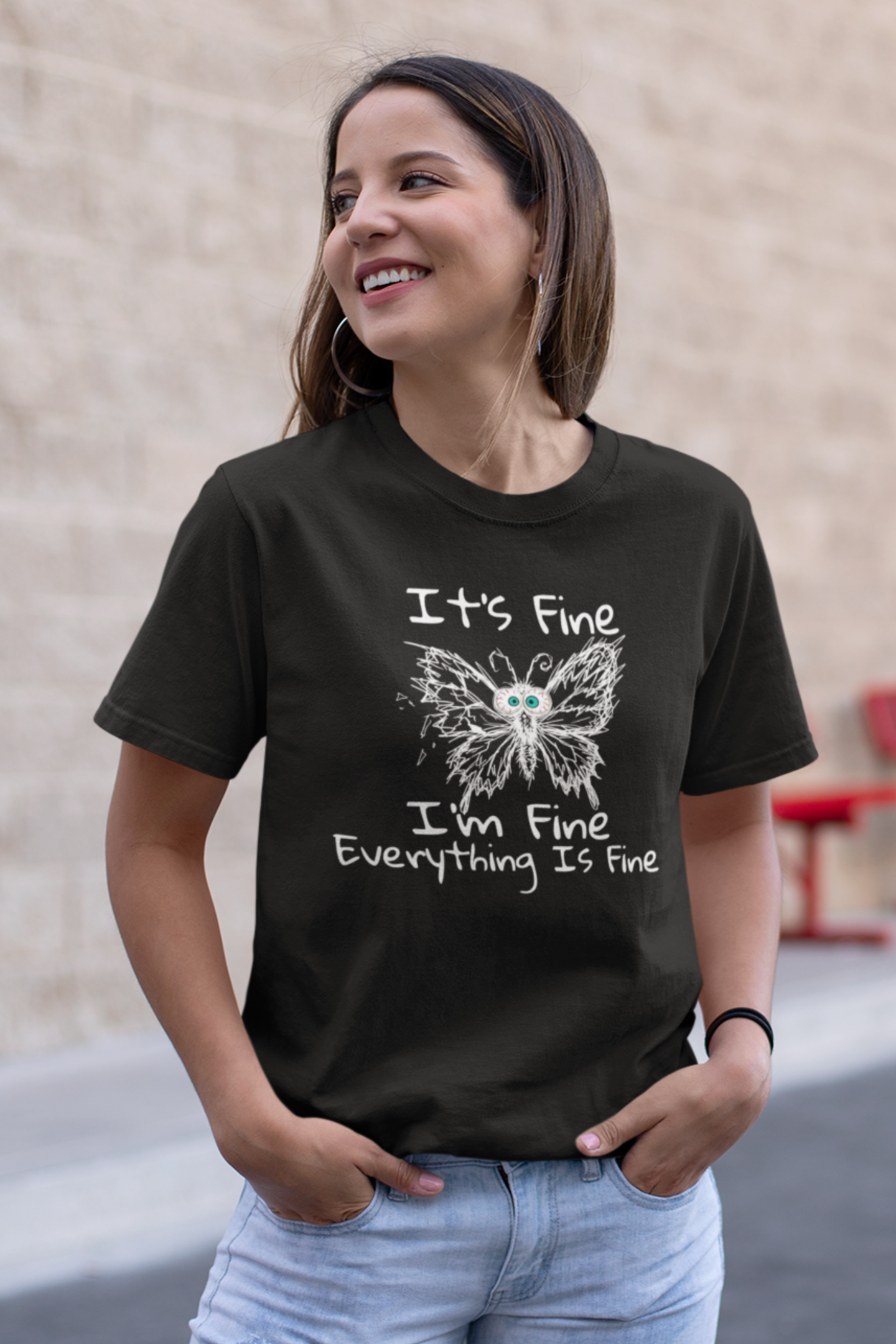 Woman wearing black It's Fine I'm Fine Everything Is Fine anxious butterfly graphic t-shirt, standing against a beige wall.