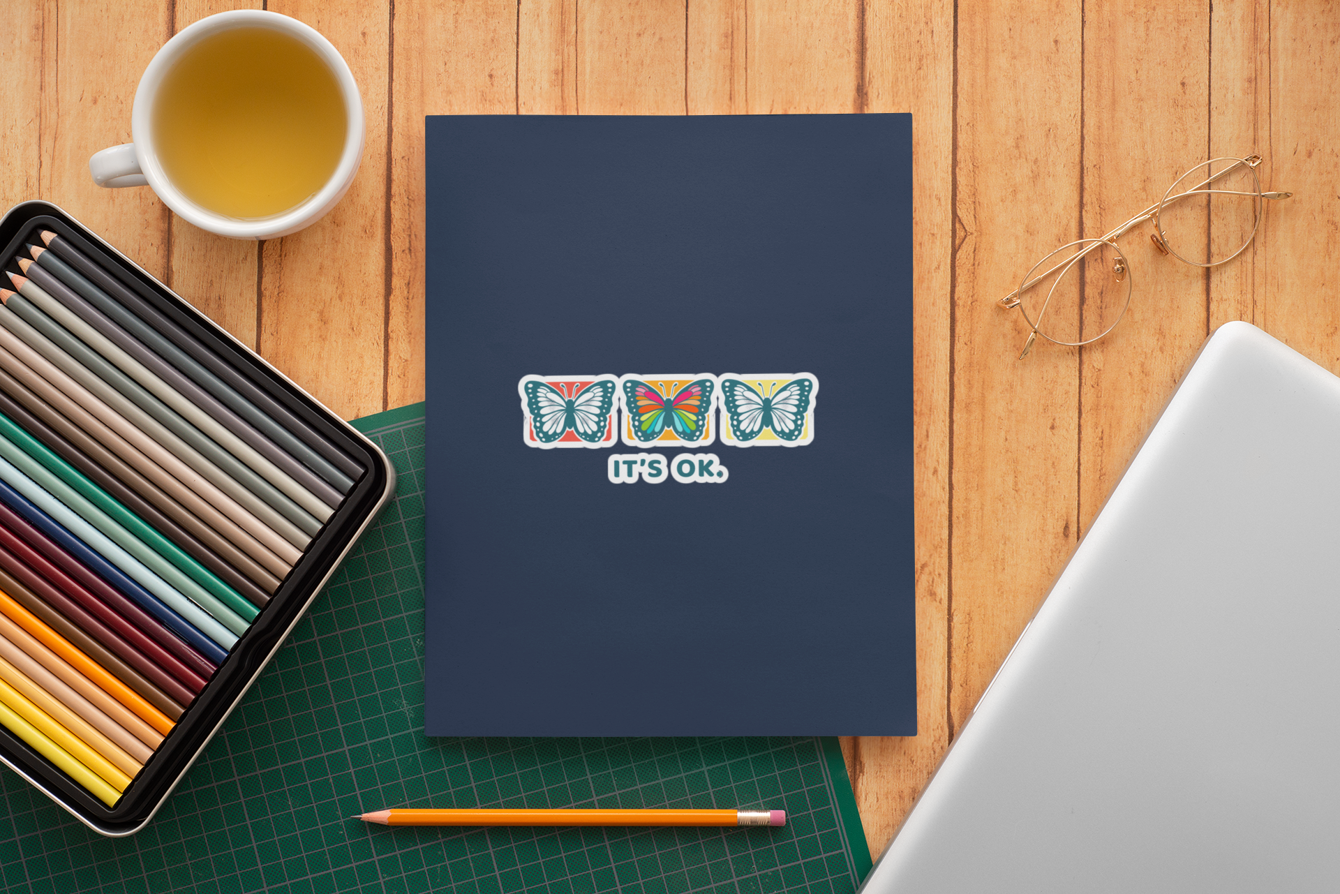 'it's ok' rainbow butterfly sticker on a spiral notebook, desk flat-lay