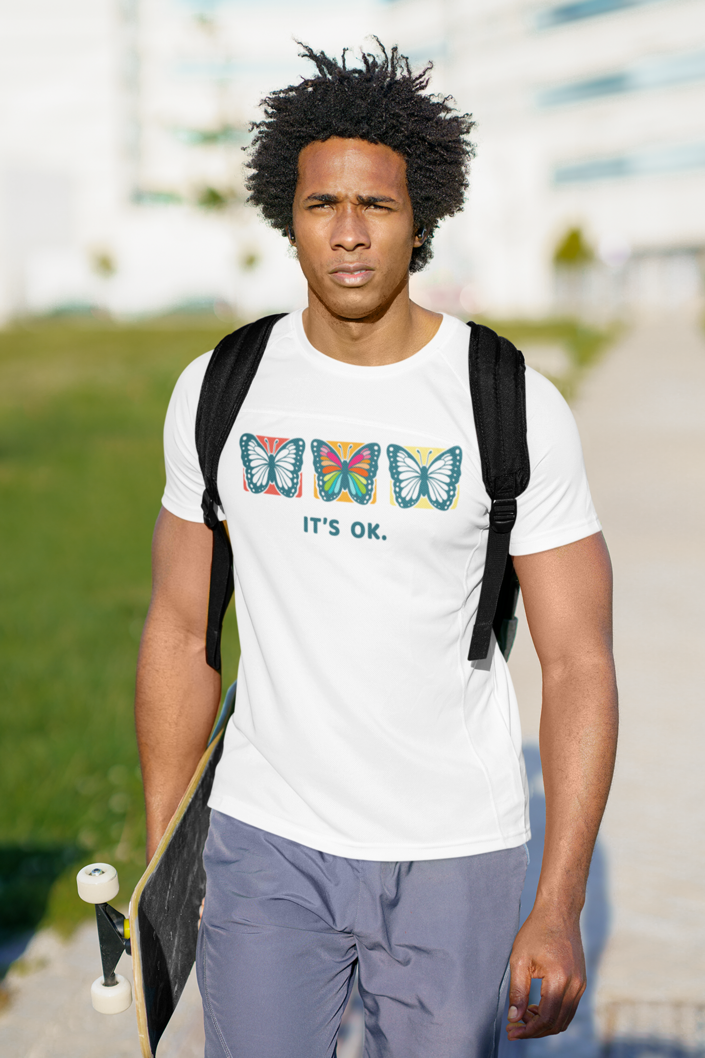a male fashion model with a backpack holding a skateboard wearing an It’s OK butterfly white shirt