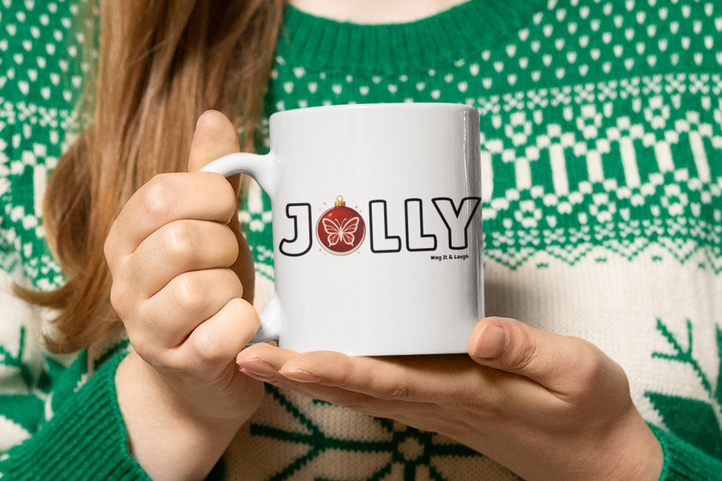 Person holding a white Christmas mug with 'Jolly' printed on it, wearing a green sweater with a pattern.