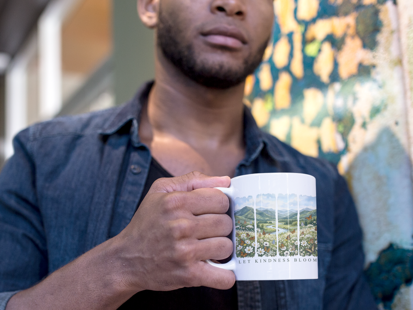 Man holding a Let Kindness Bloom butterfly floral ceramic mug in an indoor setting