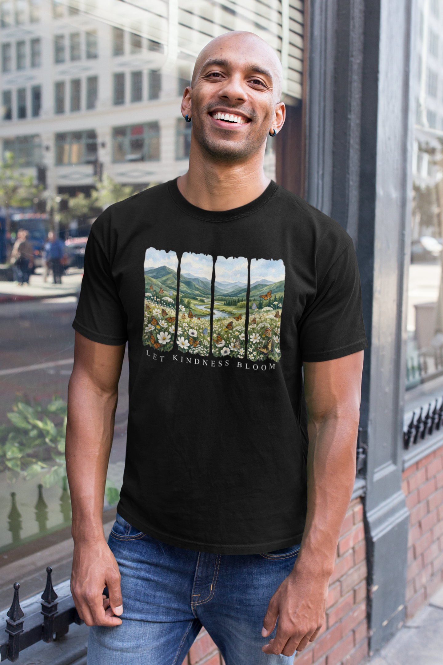 Man wearing a black Let Kindness Bloom butterfly floral landscape t-shirt in an urban setting.