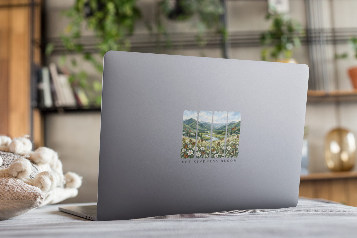 Laptop decorated with a Let Kindness Bloom floral butterfly sticker on a surface with a blurred indoor background