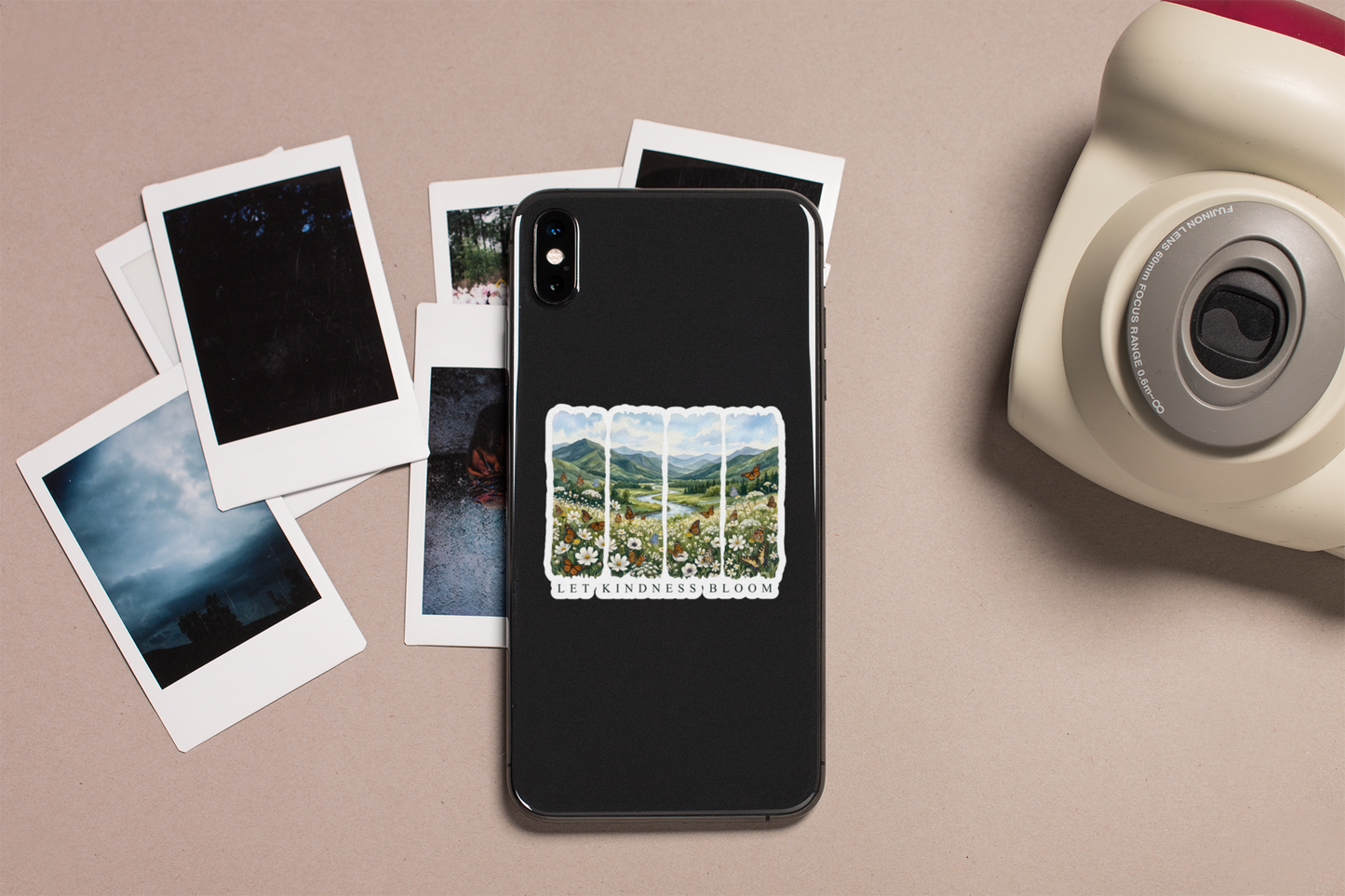 Phone case with Let Kindness Bloom butterfly floral sticker next to instant photos and a camera on a beige background