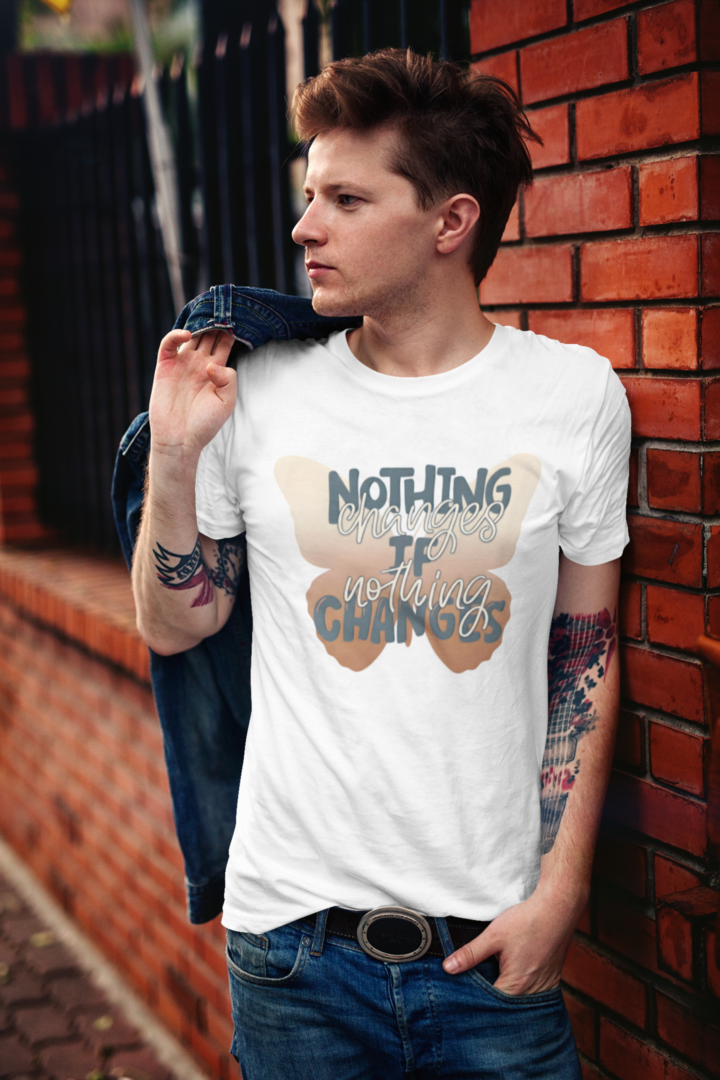 Man wearing inspirational butterfly transformation shirt nothing changes if nothing changes quote leaning against a brick wall.