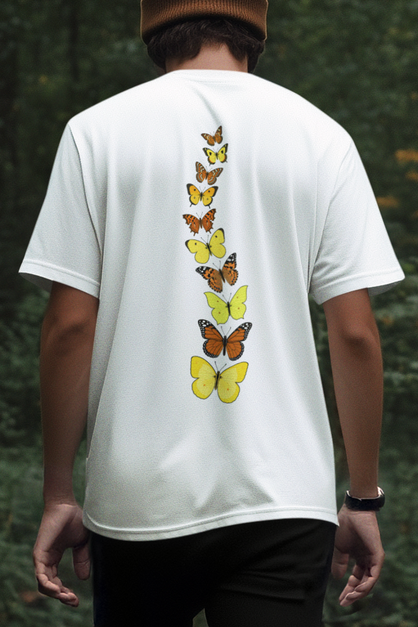 Man wearing a white butterfly graphic t-shirt with a yellow and orange butterfly back design in a forest setting.
