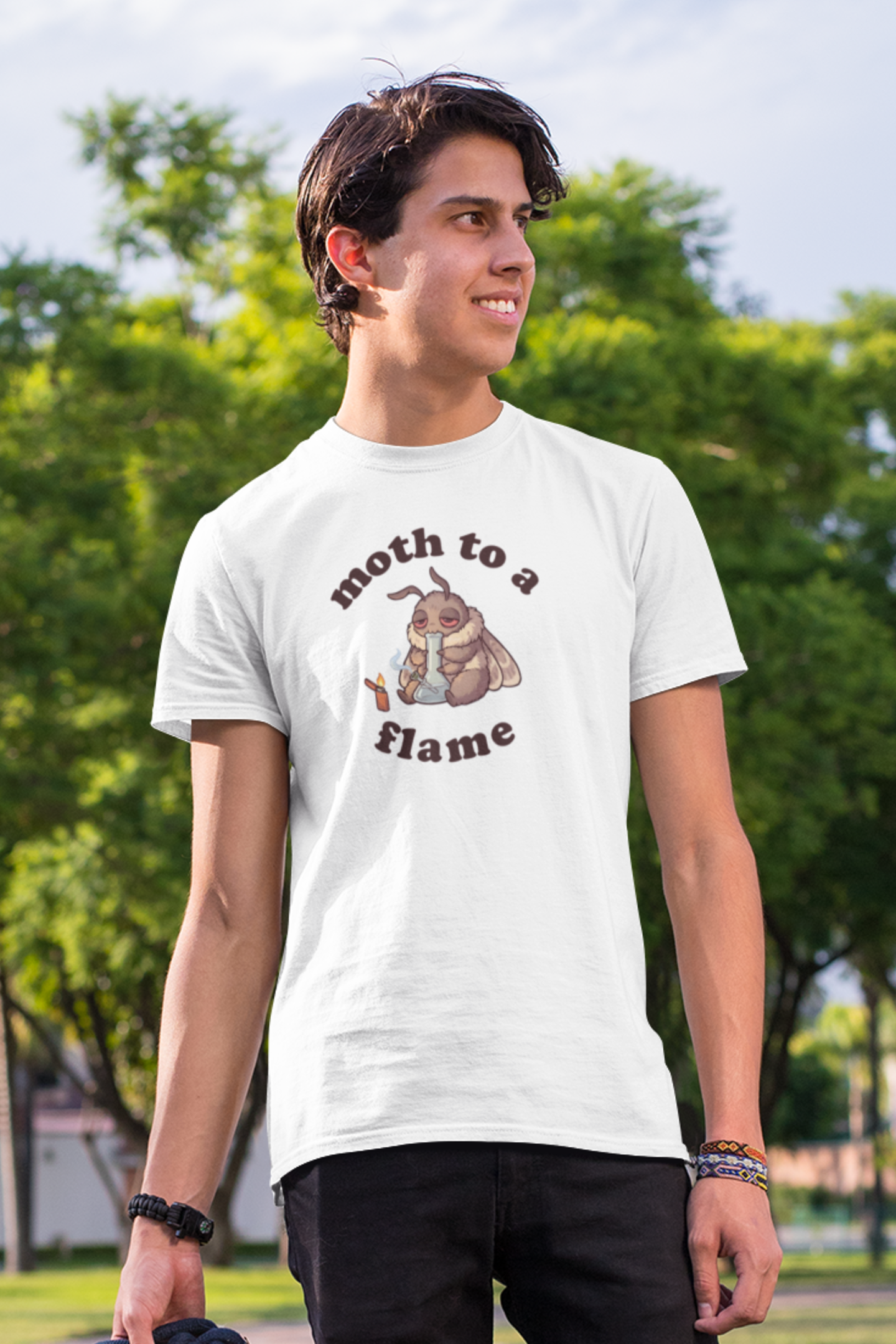 Man wearing white Moth To a Flame marijuana graphic t-shirt outdoors, funny stoner animal tee with moth, bong, and lighter design for cannabis lovers.