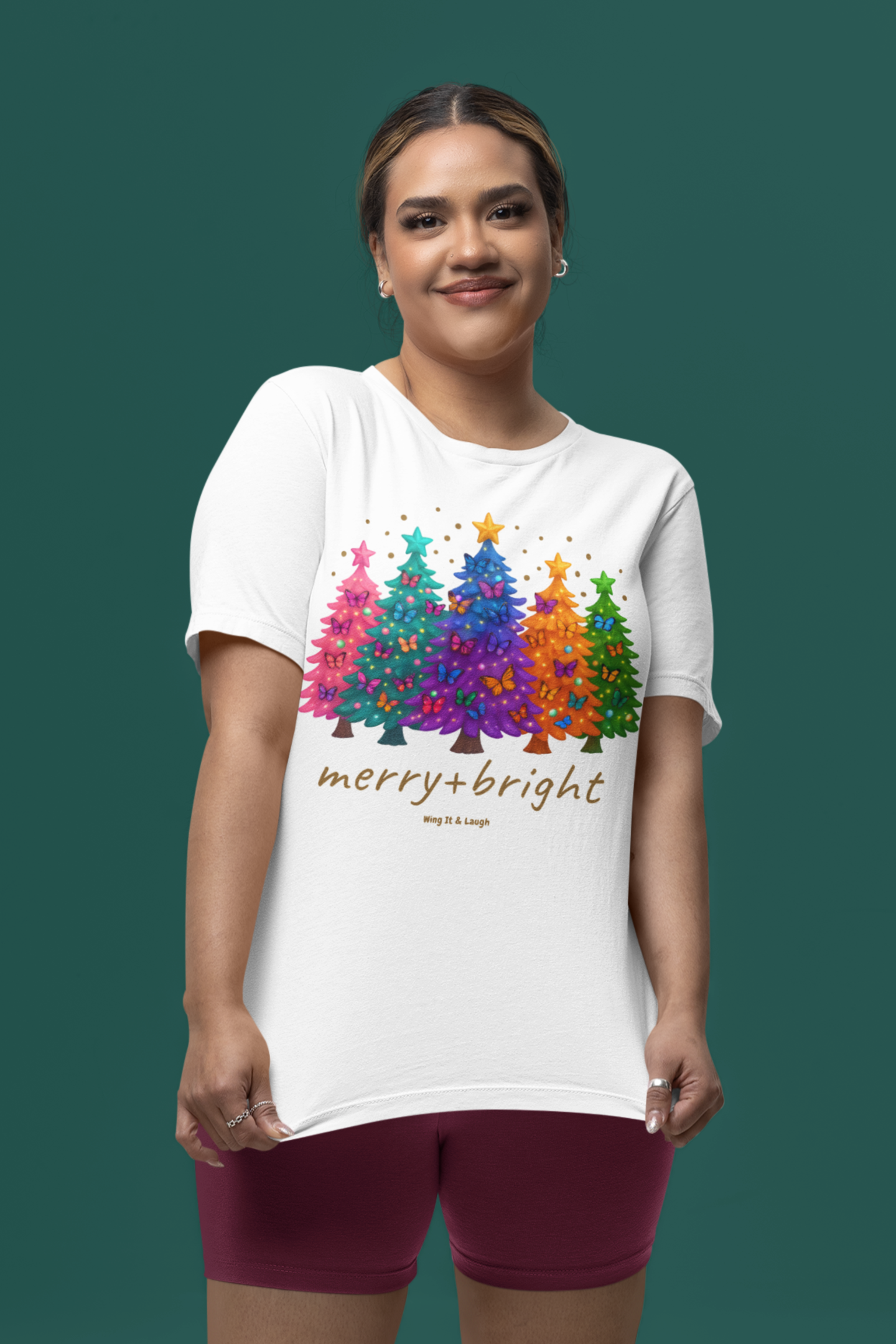 Woman wearing a white t-shirt with colorful Christmas tree design and 'merry and bright' text on a green background