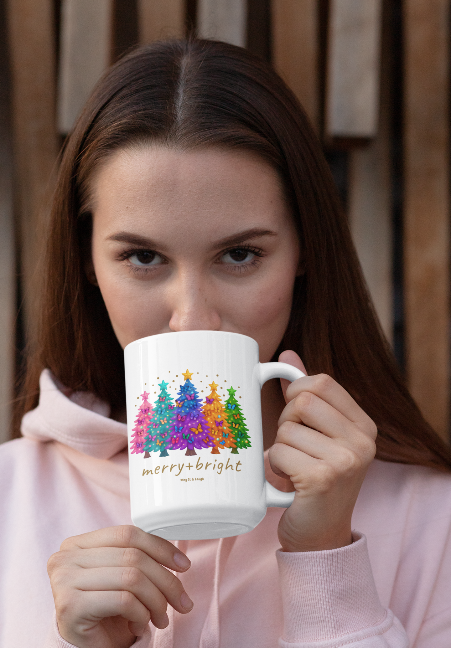 Woman holding a 15oz mug with colorful butterfly and Christmas trees design and 'merry bright' text.