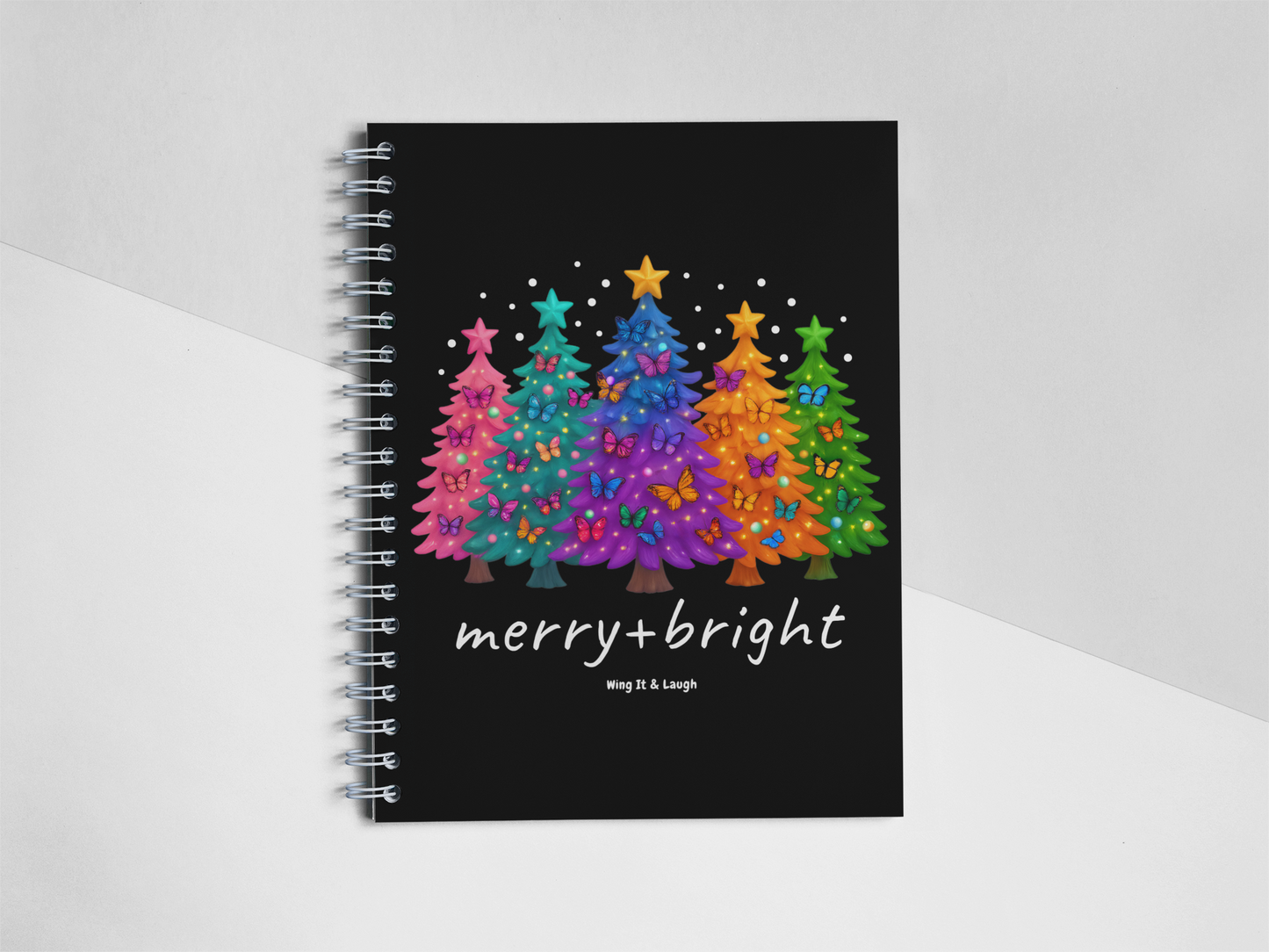 Notebook with colorful Christmas trees design and 'merry + bright' text on a white and gray background