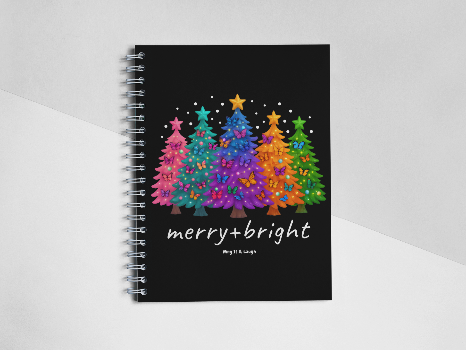 Notebook with colorful Christmas trees design and 'merry + bright' text on a white and gray background
