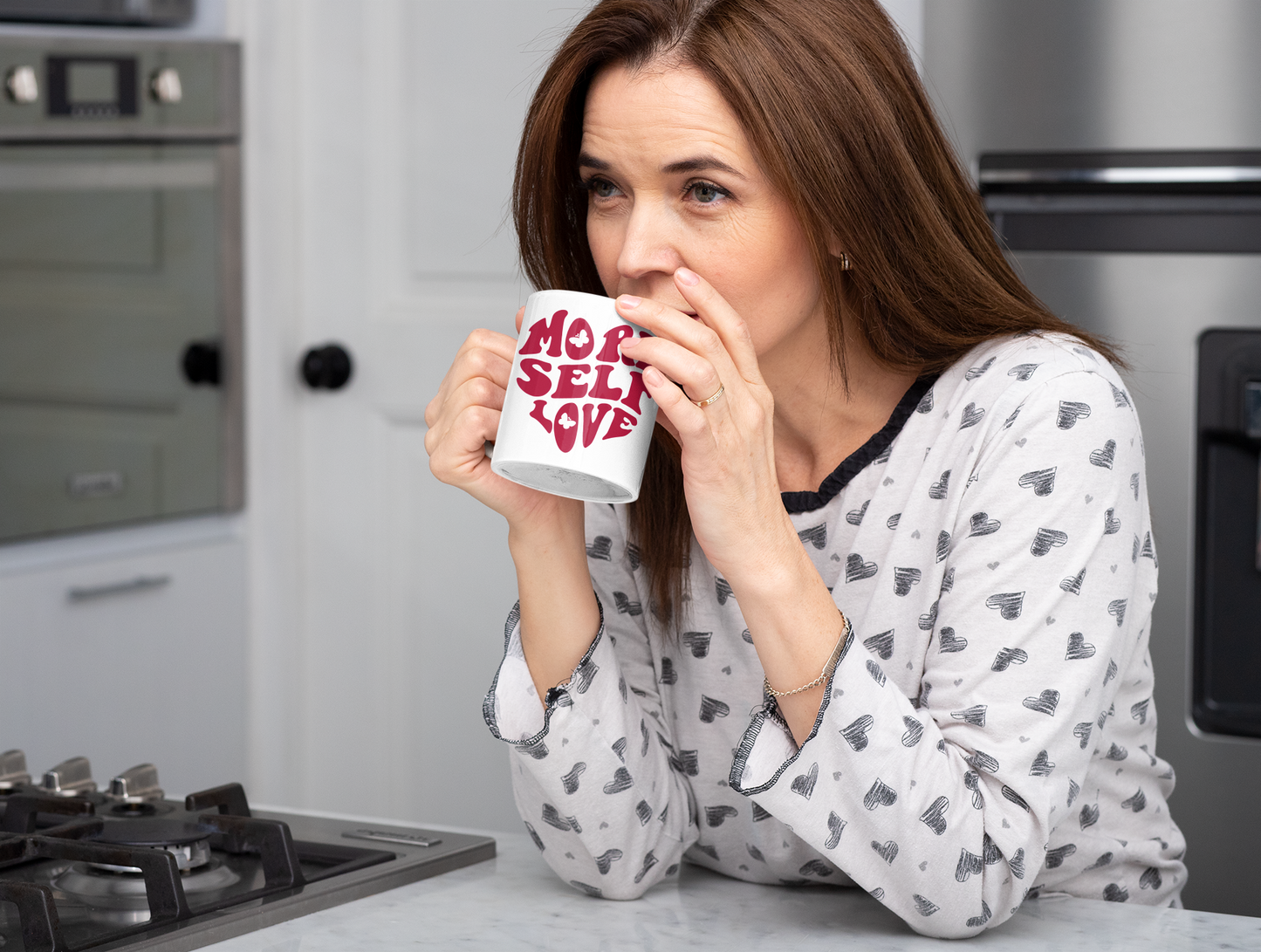 Woman drinking from More Self Love butterfly Valentine mug in a kitchen.