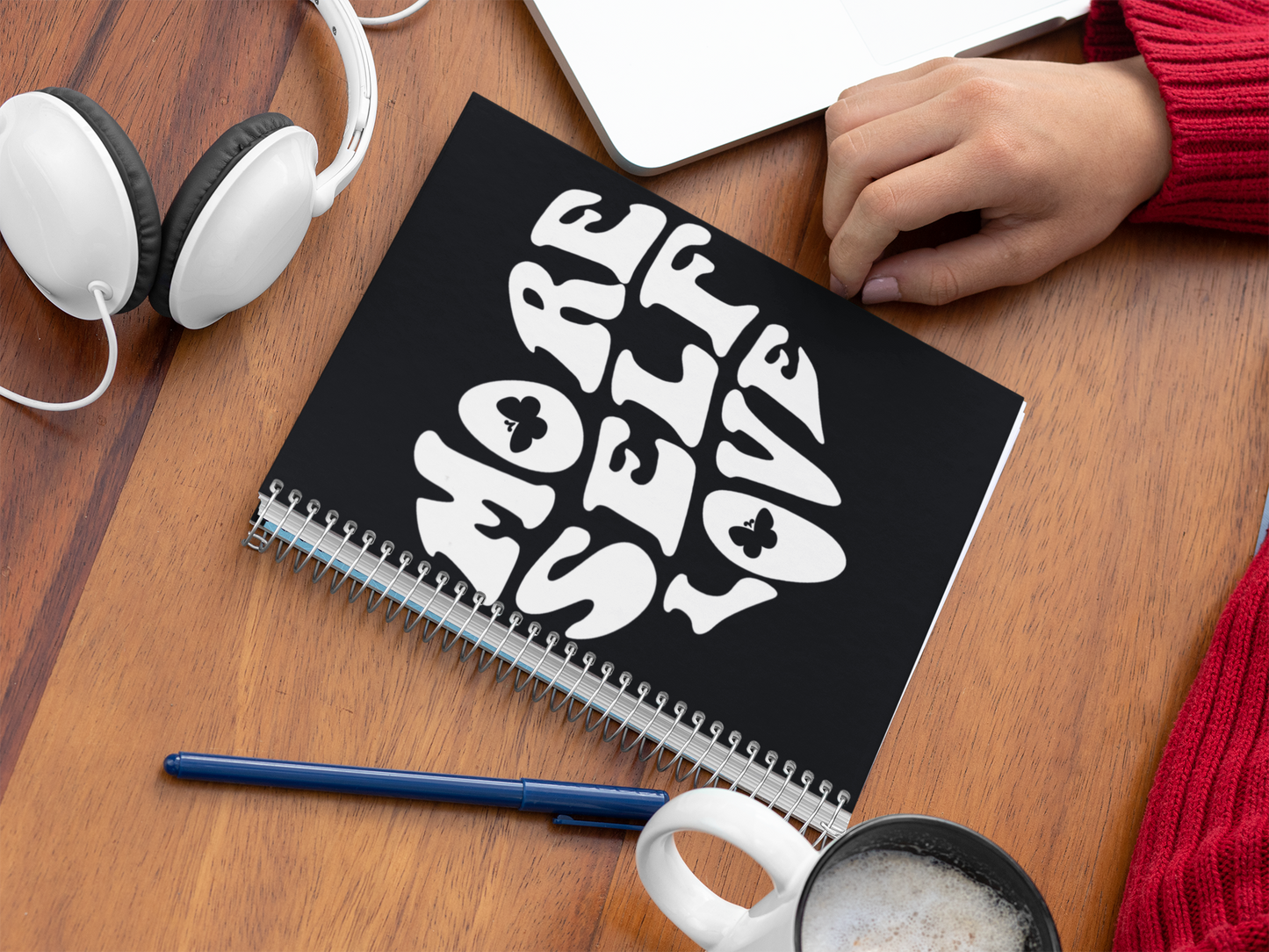 More Self Love spiral notebook on a wooden table with headphones and a mug.